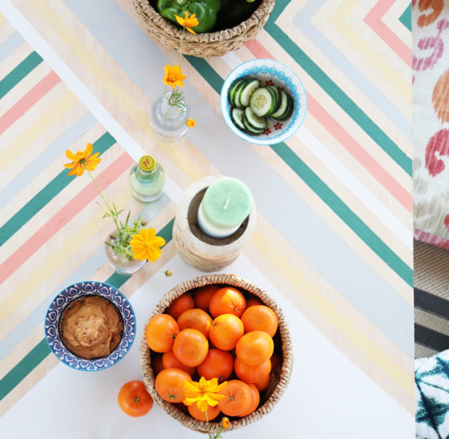 Table with pastel-colored lines. There is a bowl of bell peppers, a bowl of clementines, flowers, and a few other small items on the table.