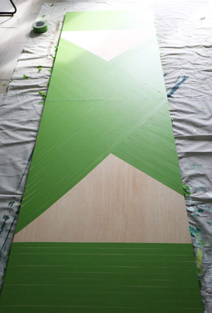 Large wooden board taped off with Green FrogTape Multi-Surface Painter's Tape. There are two open triangular sections still showing off the wood.