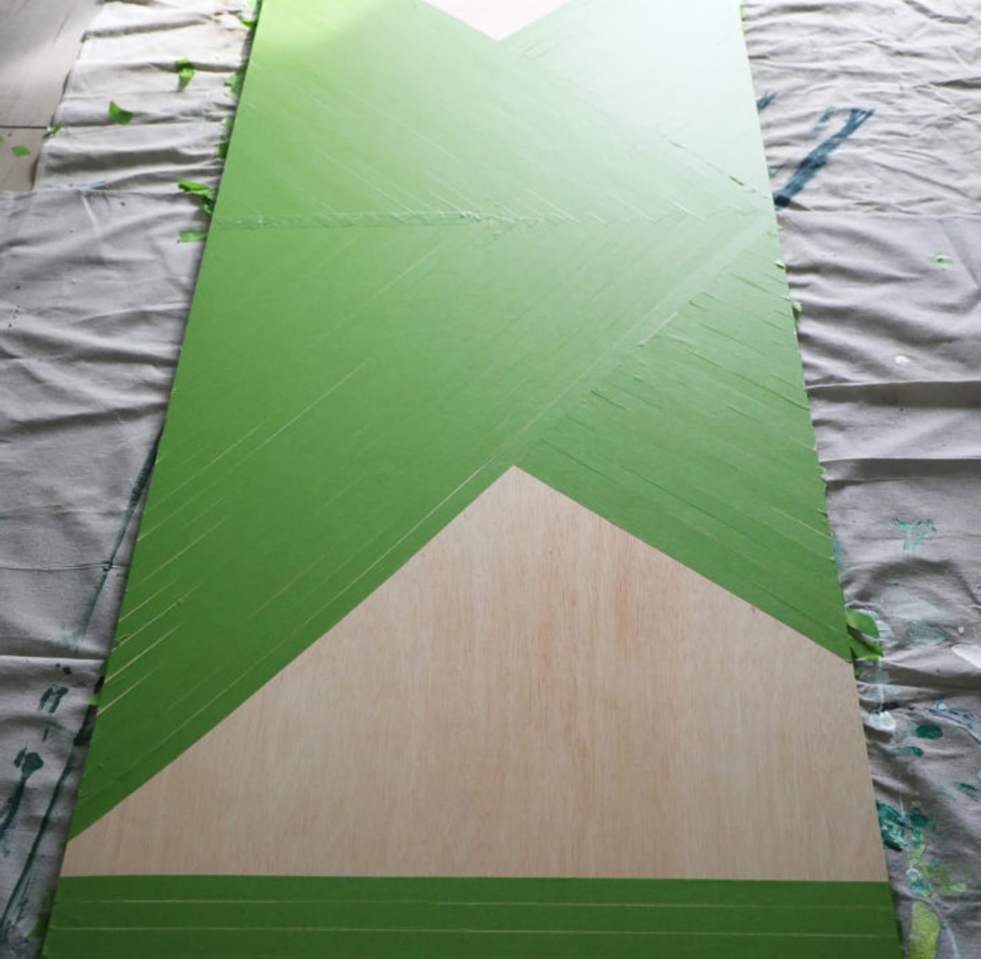 Large wooden board taped off with Green FrogTape Multi-Surface Painter's Tape. There are two open triangular sections still showing off the wood.