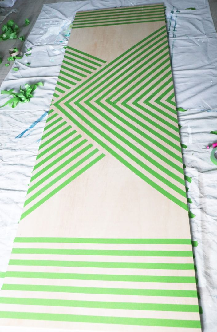 Large wooden board with multiple strips of Green FrogTape Multi-Surface Painter's Tape taped onto it. The ends are taped horizontally and the middle is taped in multiple V like strips