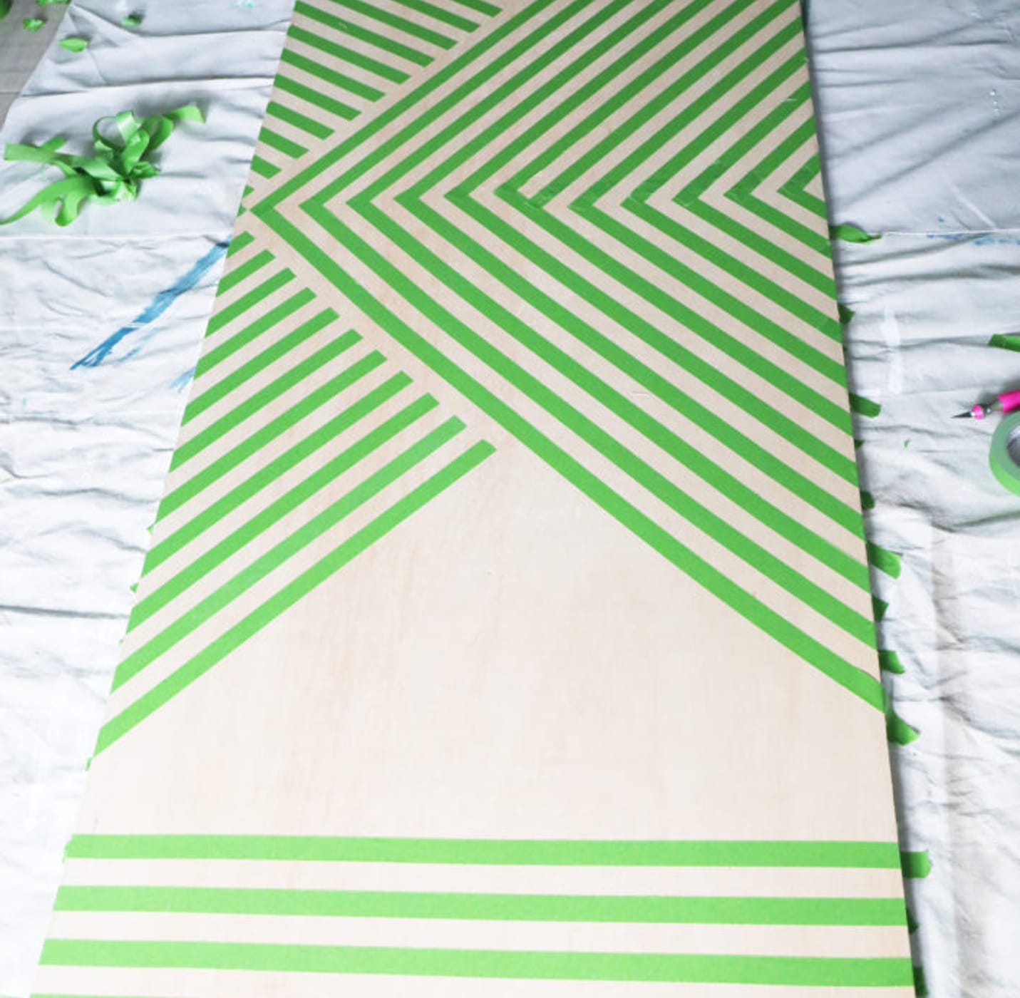 Large wooden board with multiple strips of Green FrogTape Multi-Surface Painter's Tape taped onto it. The ends are taped horizontally and the middle is taped in multiple V like strips