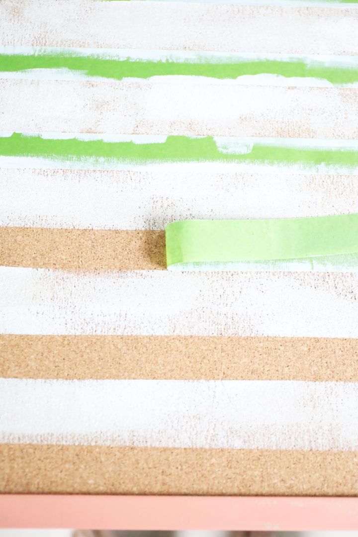 Green FrogTape Multi-Surface Painter's Tape being peeled off of a cork board.