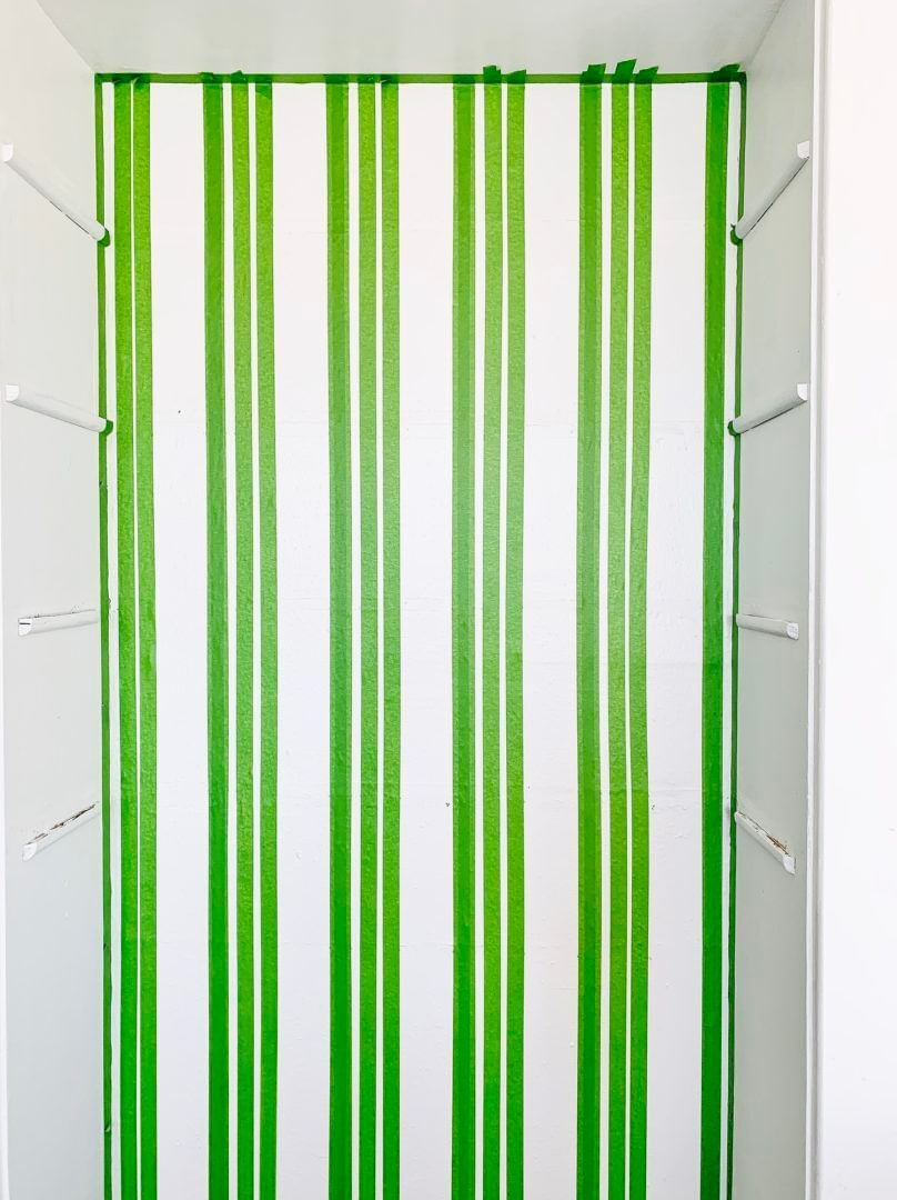 Multiple vertical strips of Green FrogTape Multi-Surface Painter's Tape on a white wall running from ceiling to floor.