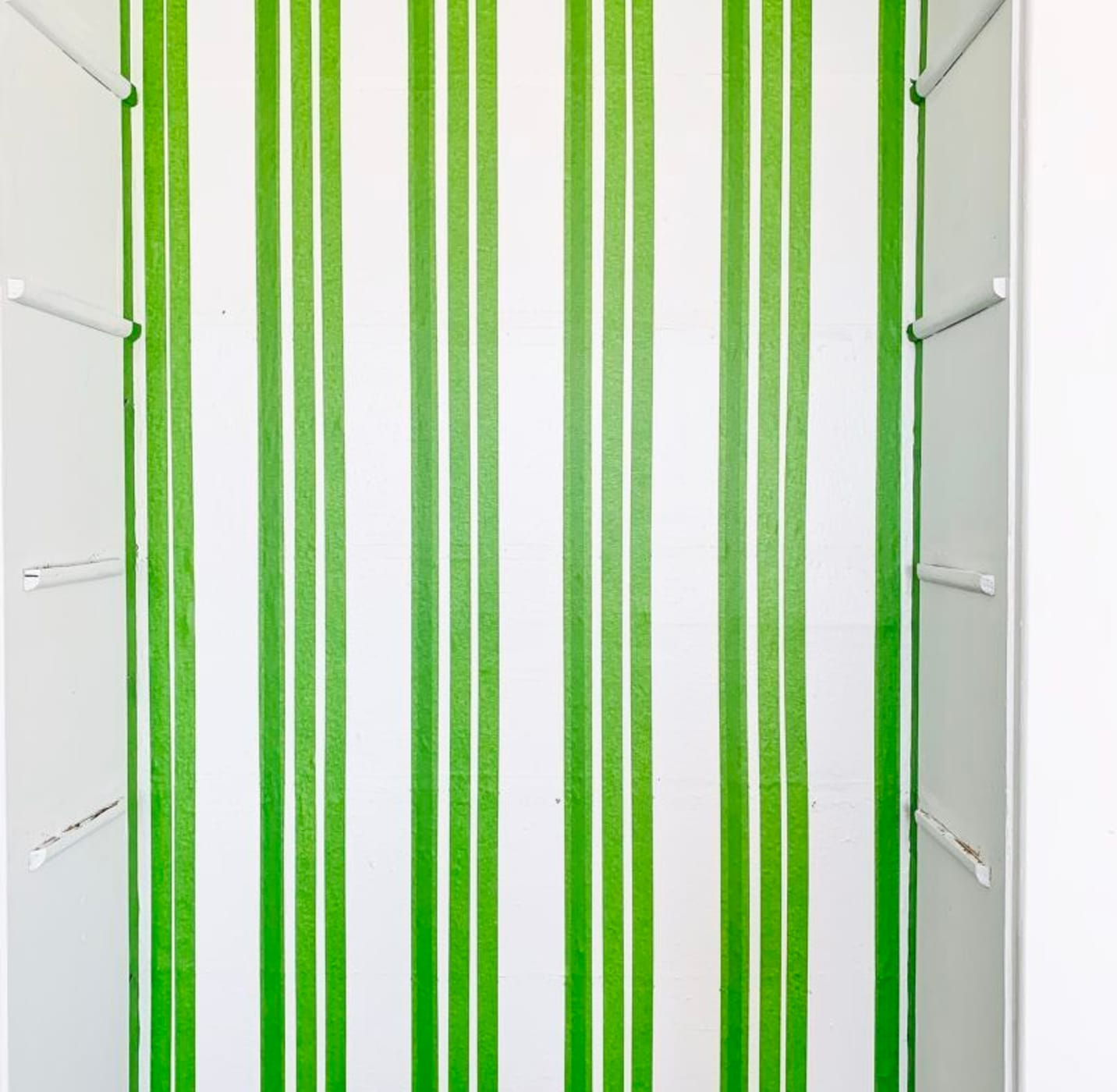 Multiple vertical strips of Green FrogTape Multi-Surface Painter's Tape on a white wall running from ceiling to floor.
