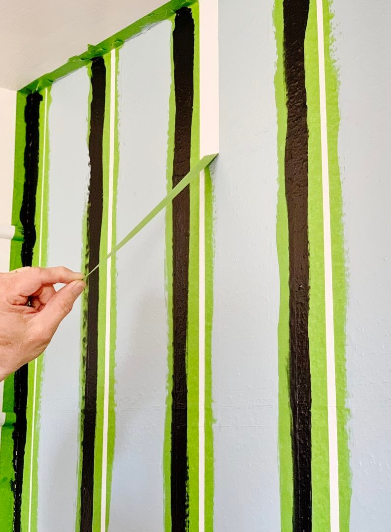 Vertical strips of Green FrogTape Multi-Surface Painter's Tape on a wall with one being pulled off to reveal a crisp white line.