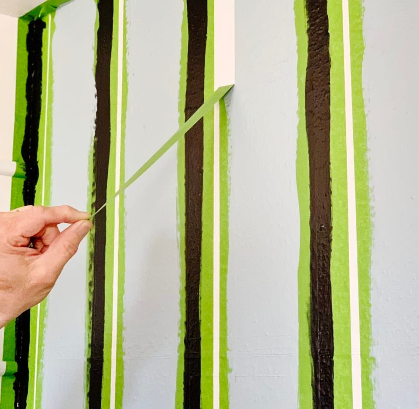 Vertical strips of Green FrogTape Multi-Surface Painter's Tape on a wall with one being pulled off to reveal a crisp white line.