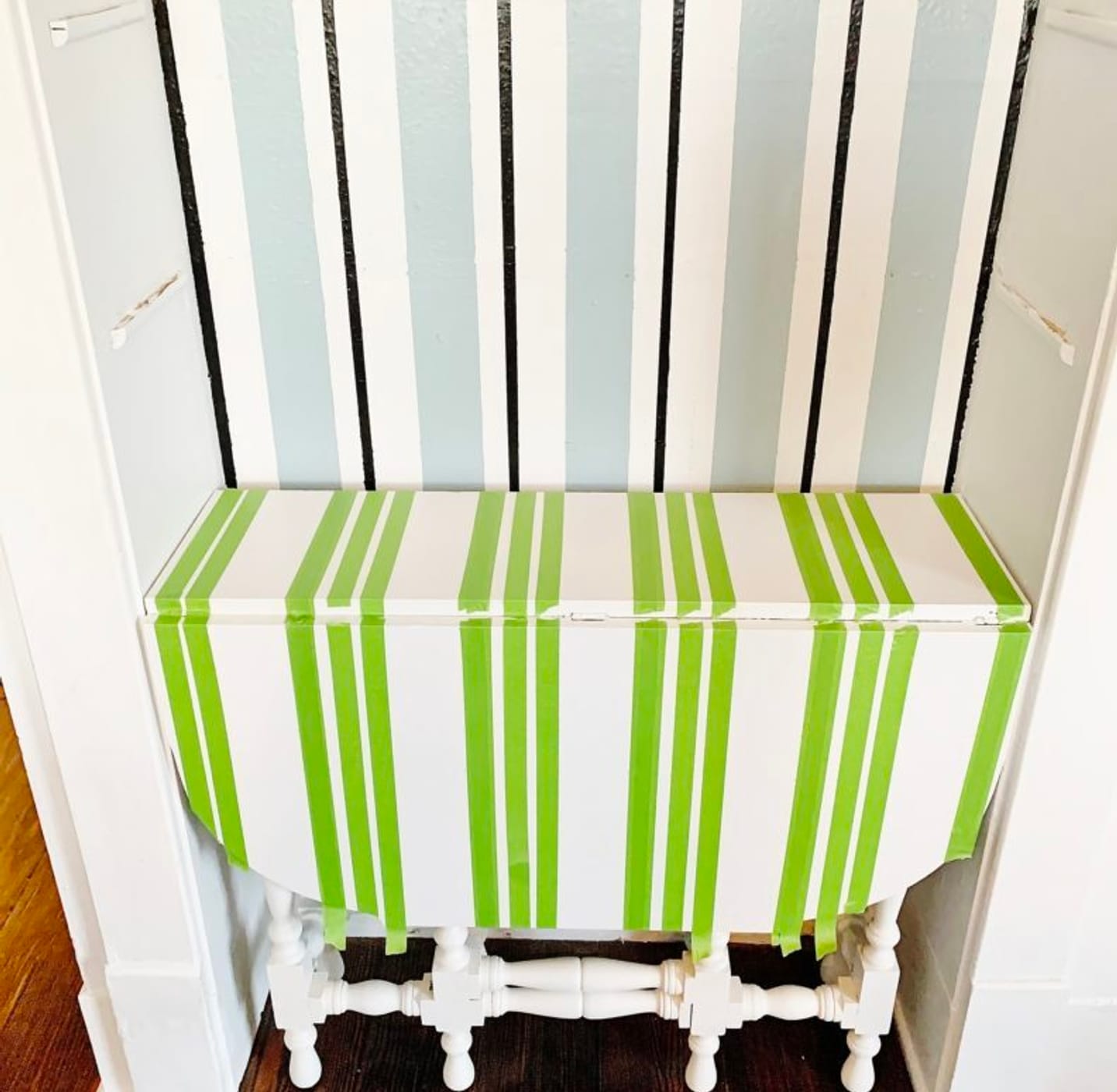 A small white table in a nook, with multiple strips of Green FrogTape Multi-Surface Painter's Tape running vertically across the table top and down the side