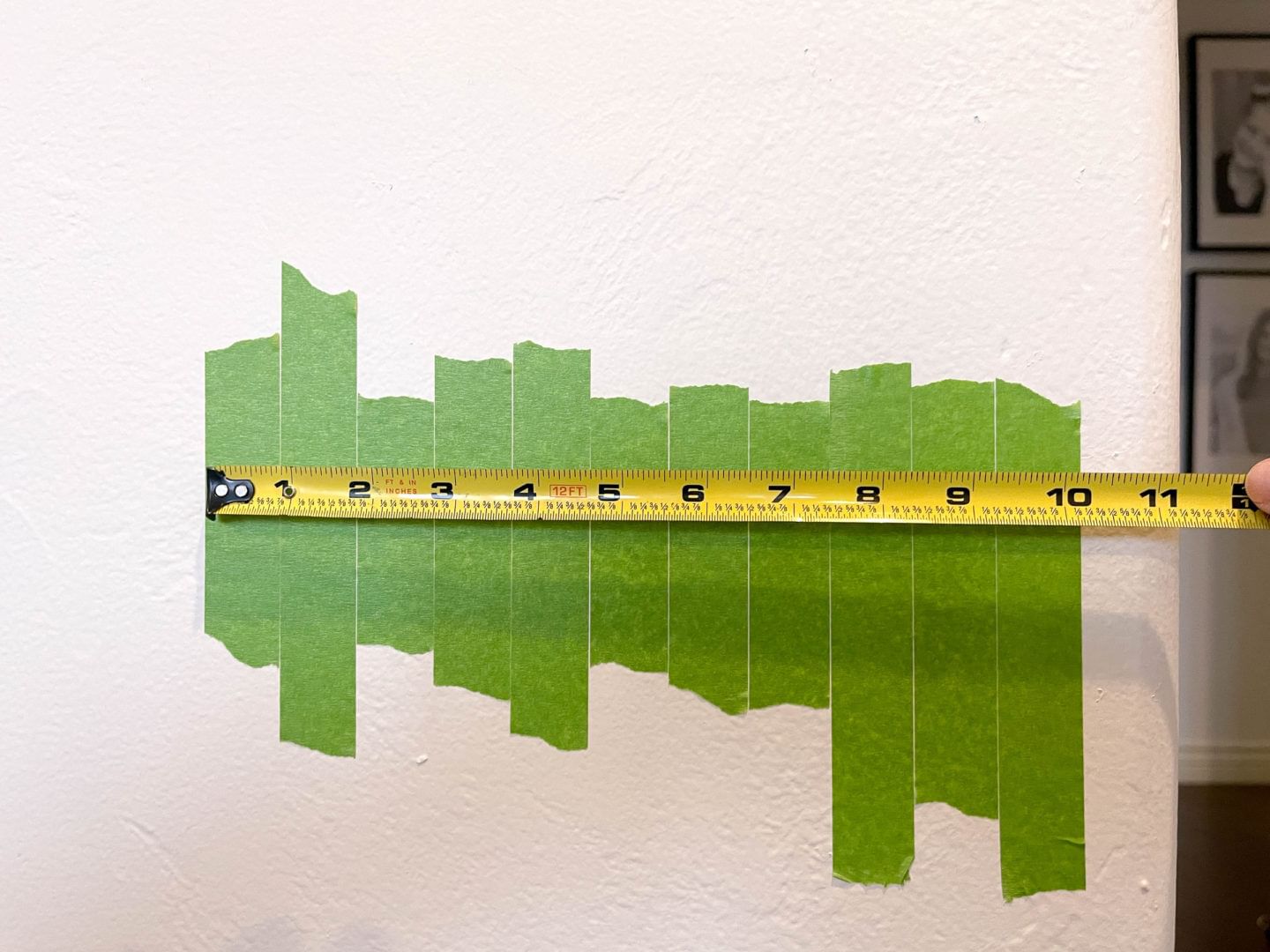 Different height strips of Green FrogTape Multi-Surface Painter's Tape on a wall next to each other with a tape measure measuring the total length. The total length shows that it is 10 inches long.