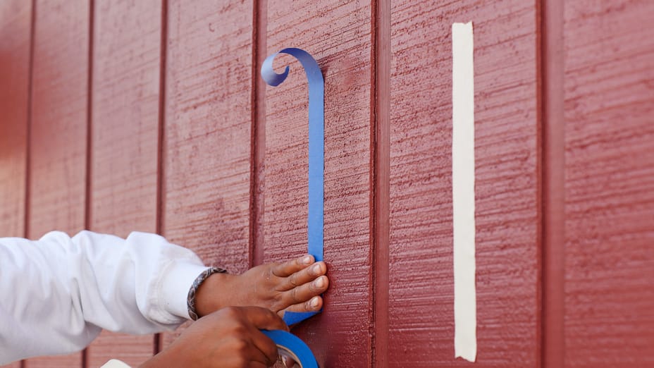 Hands taping FrogTape Pro Grade Blue Painter's Tape to the exterior of a barn wall