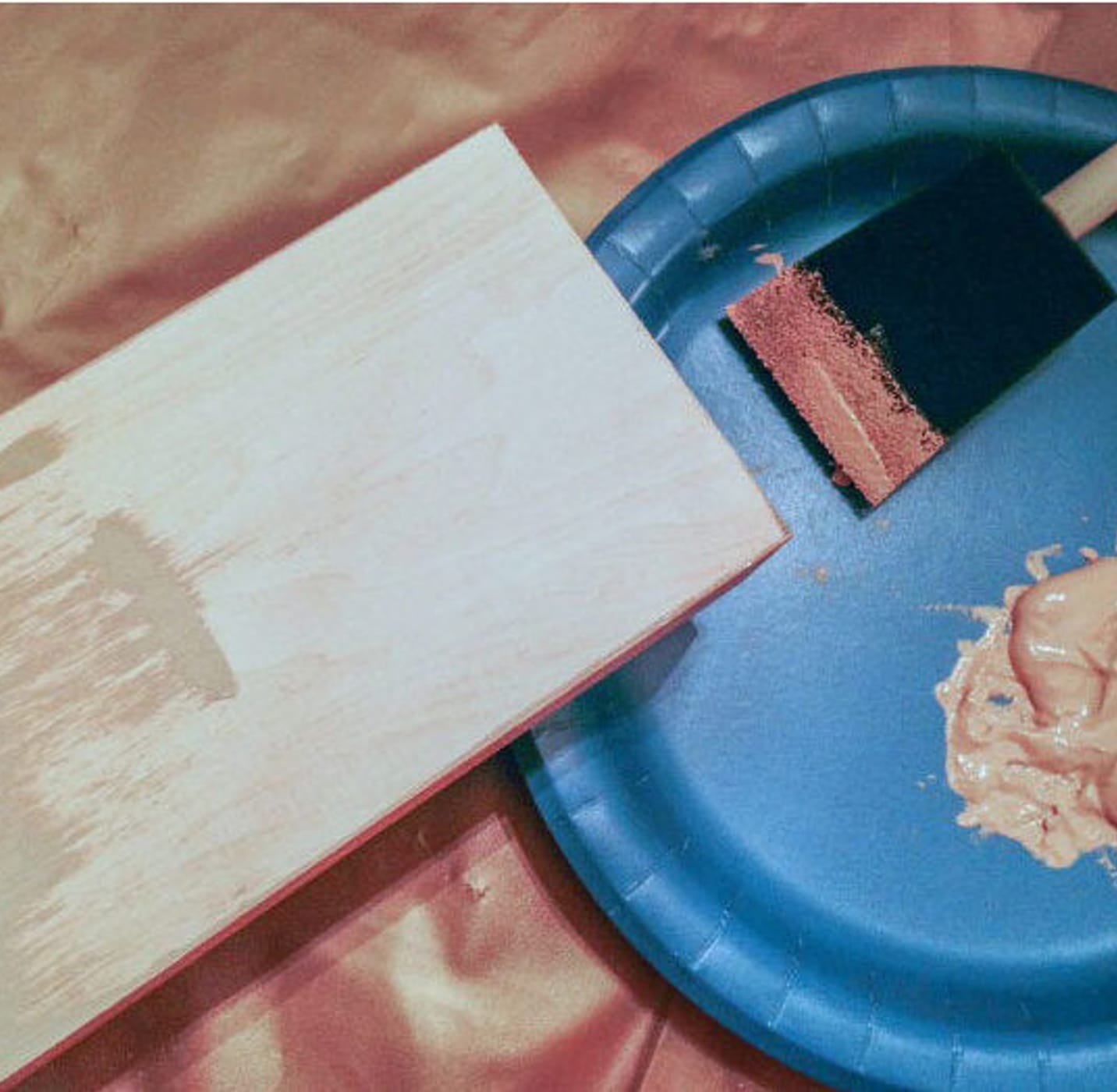 A piece of wood next to a blue plate with paint in it and a sponge brush