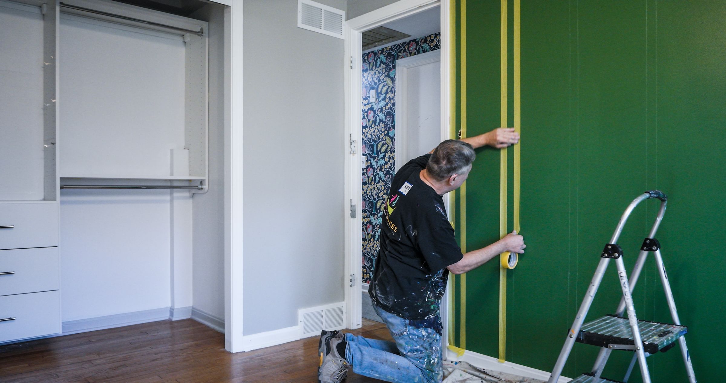 Painter taping Vertical strips of Yellow FrogTape Delicate Surface Painter's Tape to a green wall