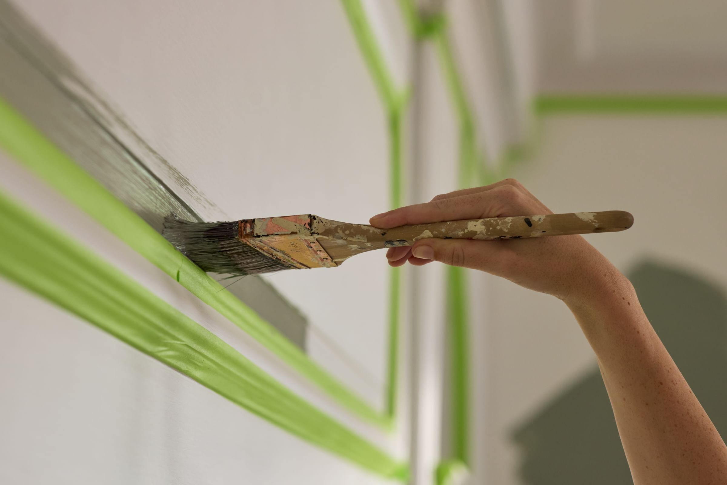 A wall being painted with a paintbrush. FrogTape Advanced is taped around the molding so there will be clean paint lines when removed