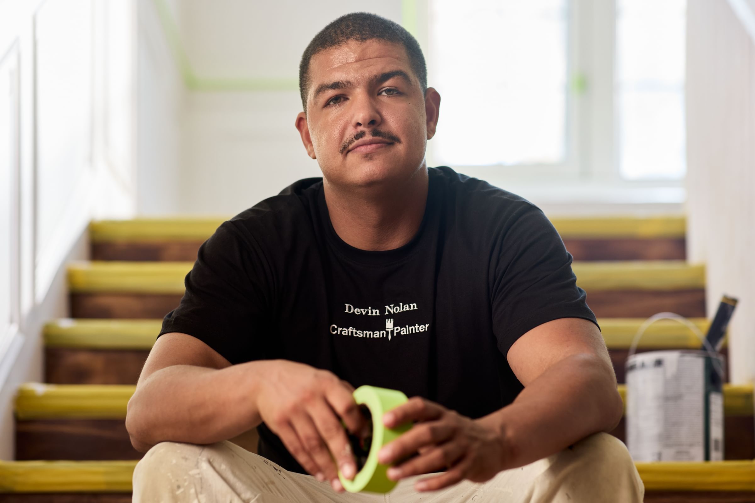 Painting Contractor sitting on steps holding a roll of green FrogTape Advanced Painter's Tape