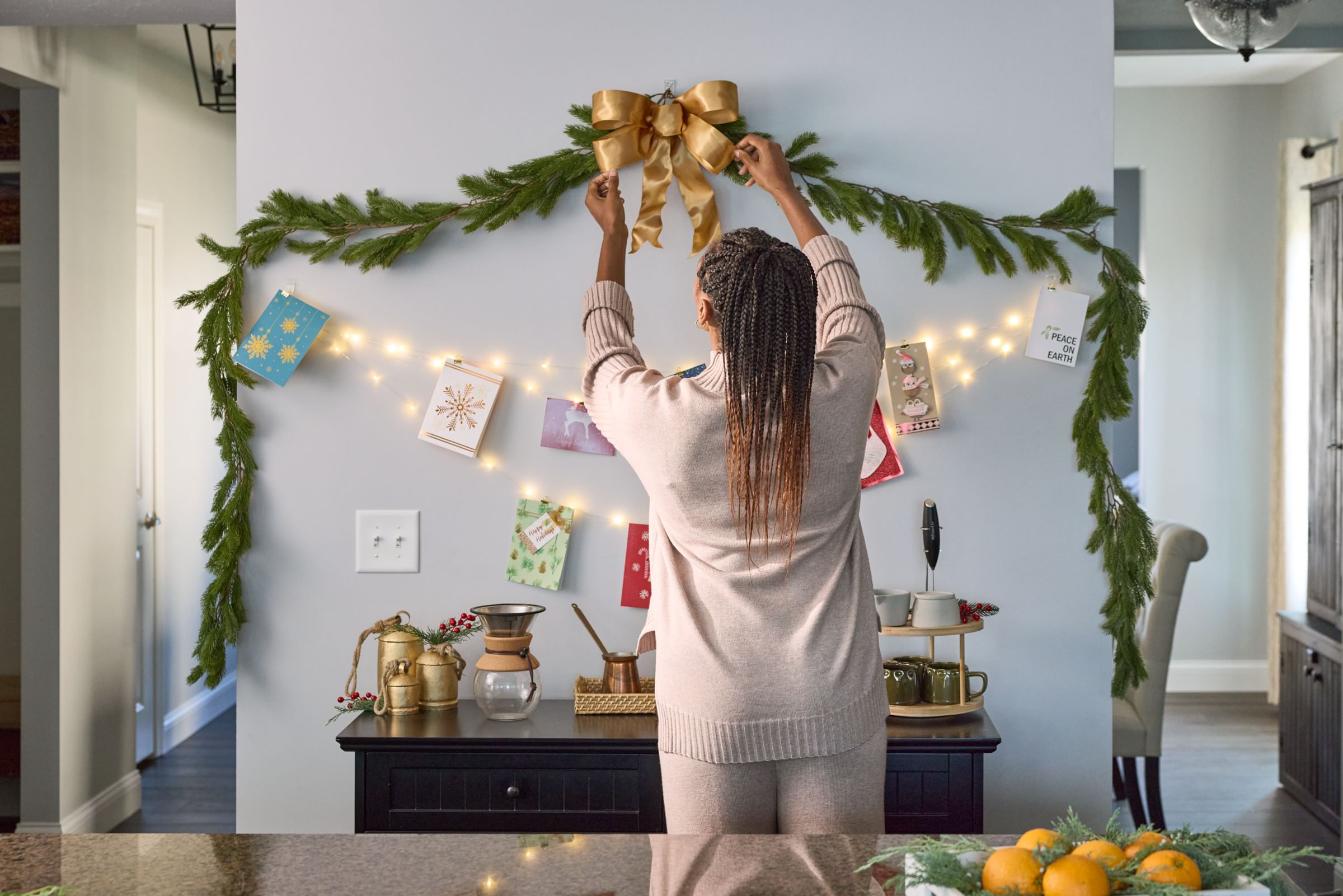 A woman hanging a gold bow on the wall around garland using FrogTape reMOVEables clear wire hooks