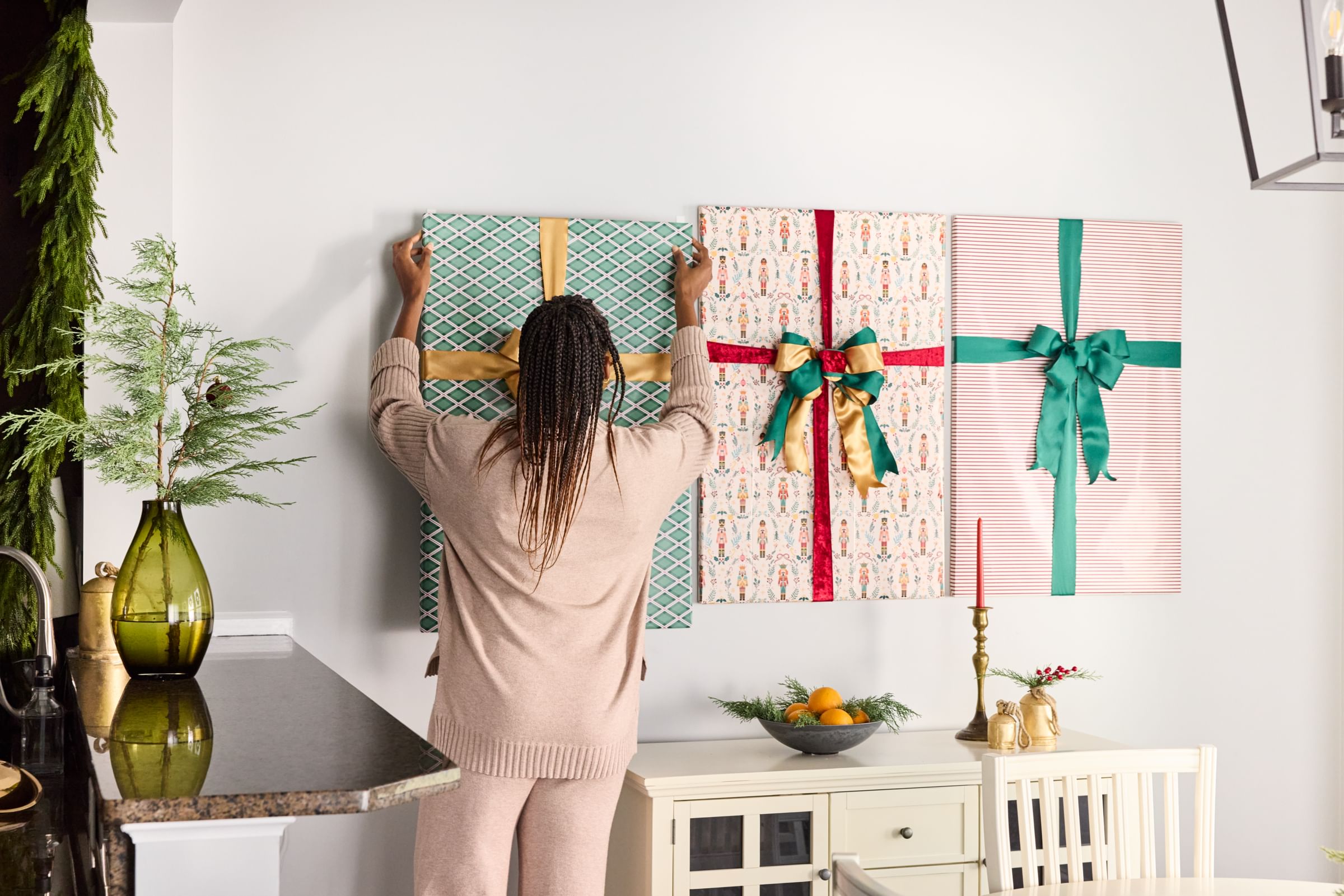 A woman hanging wrapped picture frames on a wall using FrogTape reMOVEables picture hanging hooks