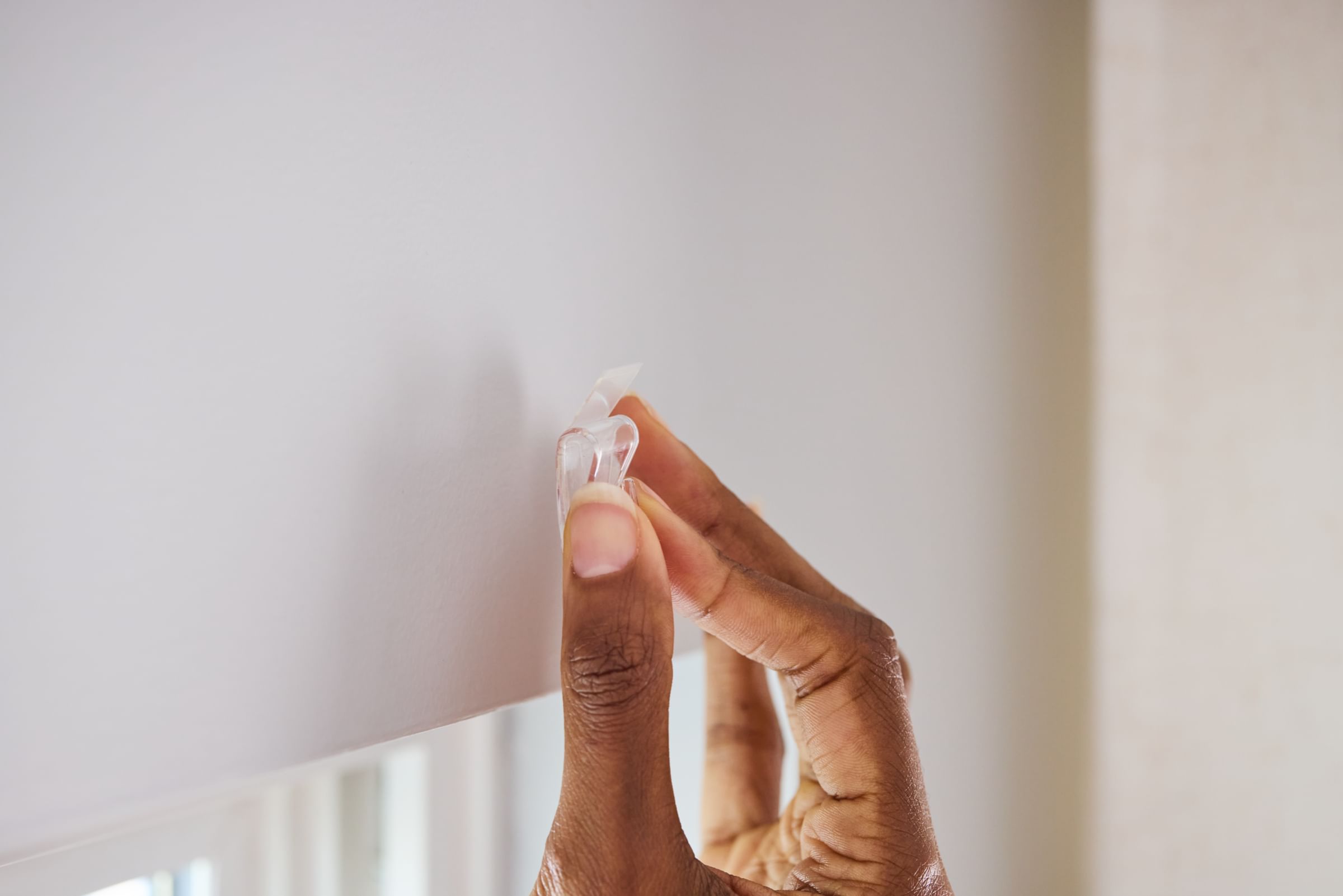 A Clear FrogTape reMOVEables mini hook being placed on a wall.