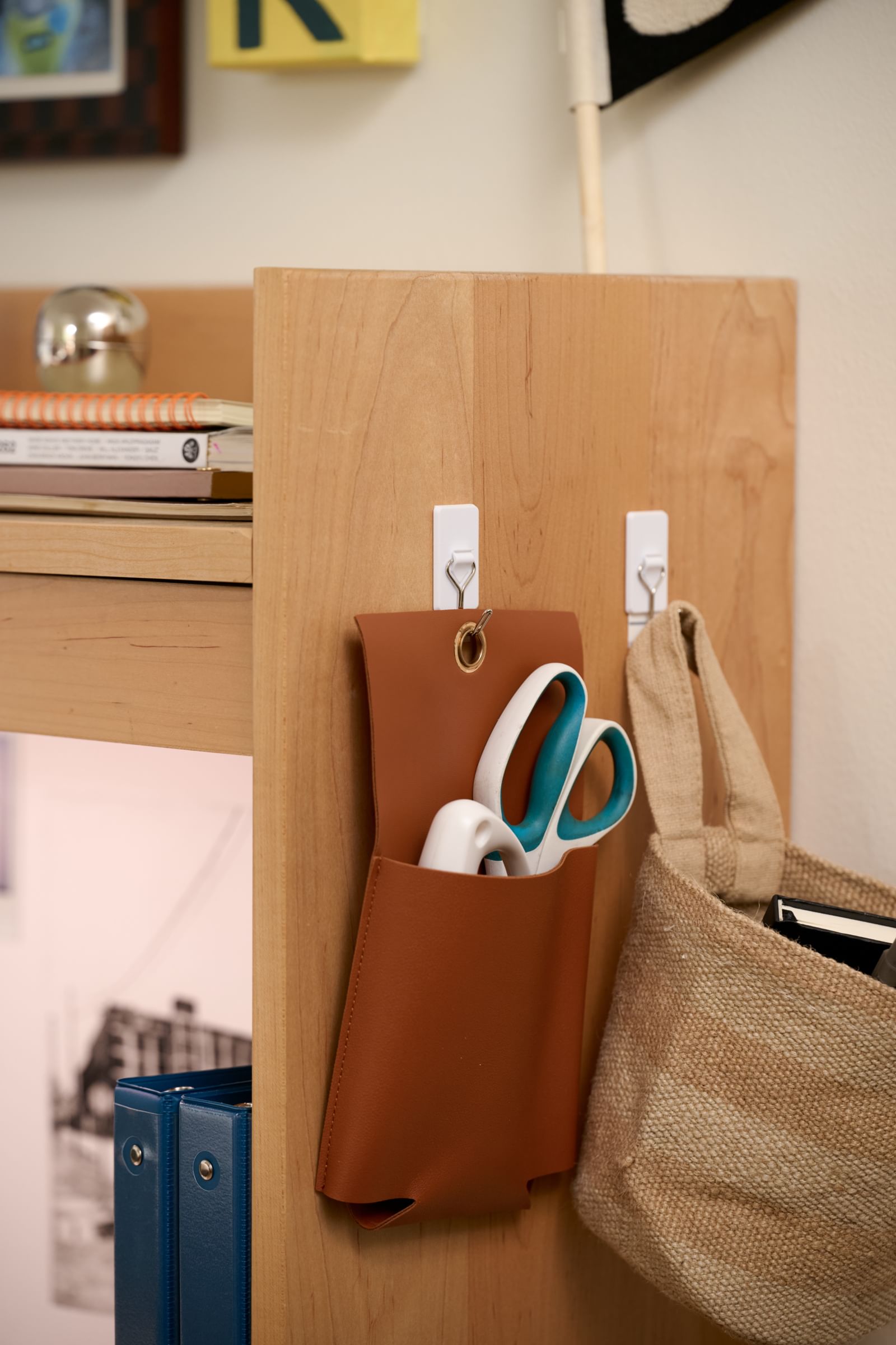 A Storage Basket and Pouch hanging on FrogTape reMOVEables wire hooks on the side of a desk