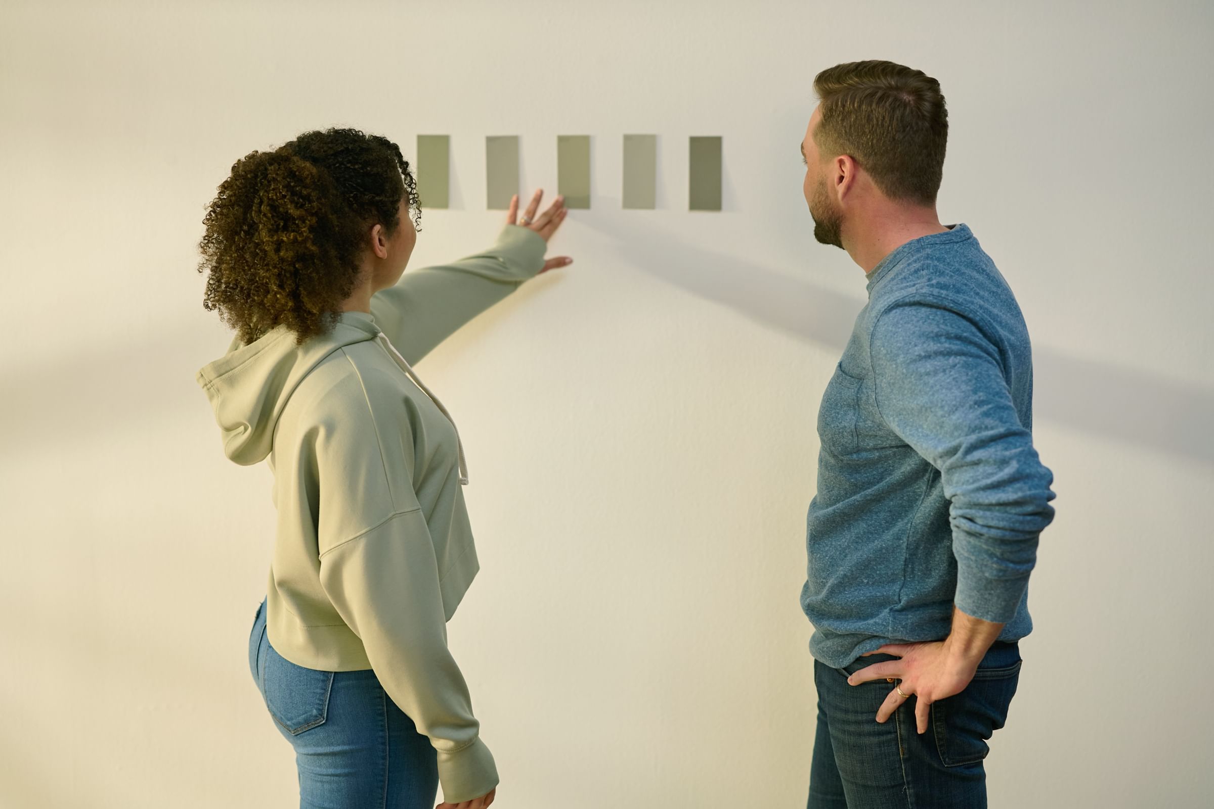 A Couple looking at different color paint chips on their wall to help determine what color to pick