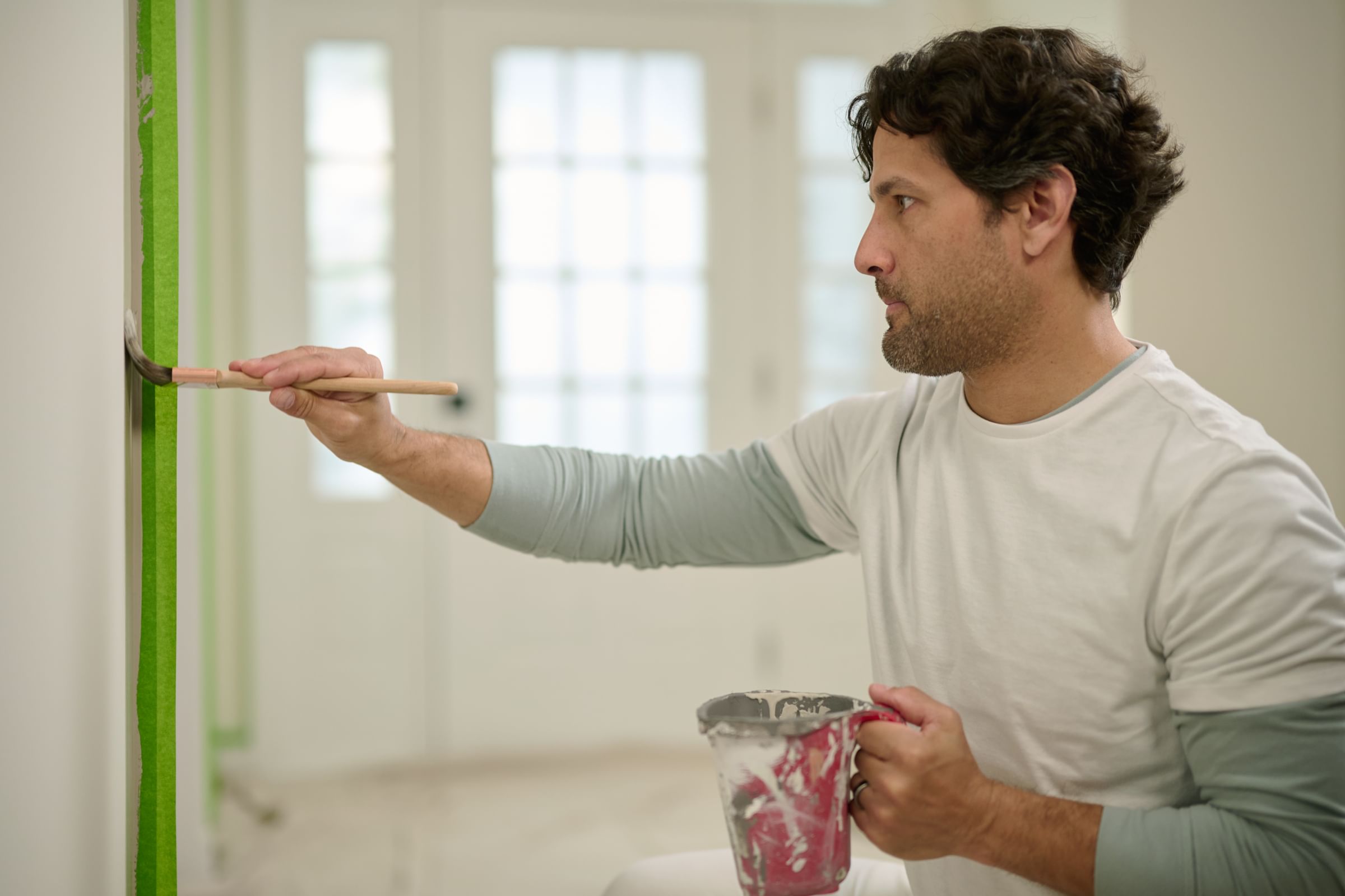 Man painting a wall taped off with Green FrogTape Multi-Surface Painter's Tape.