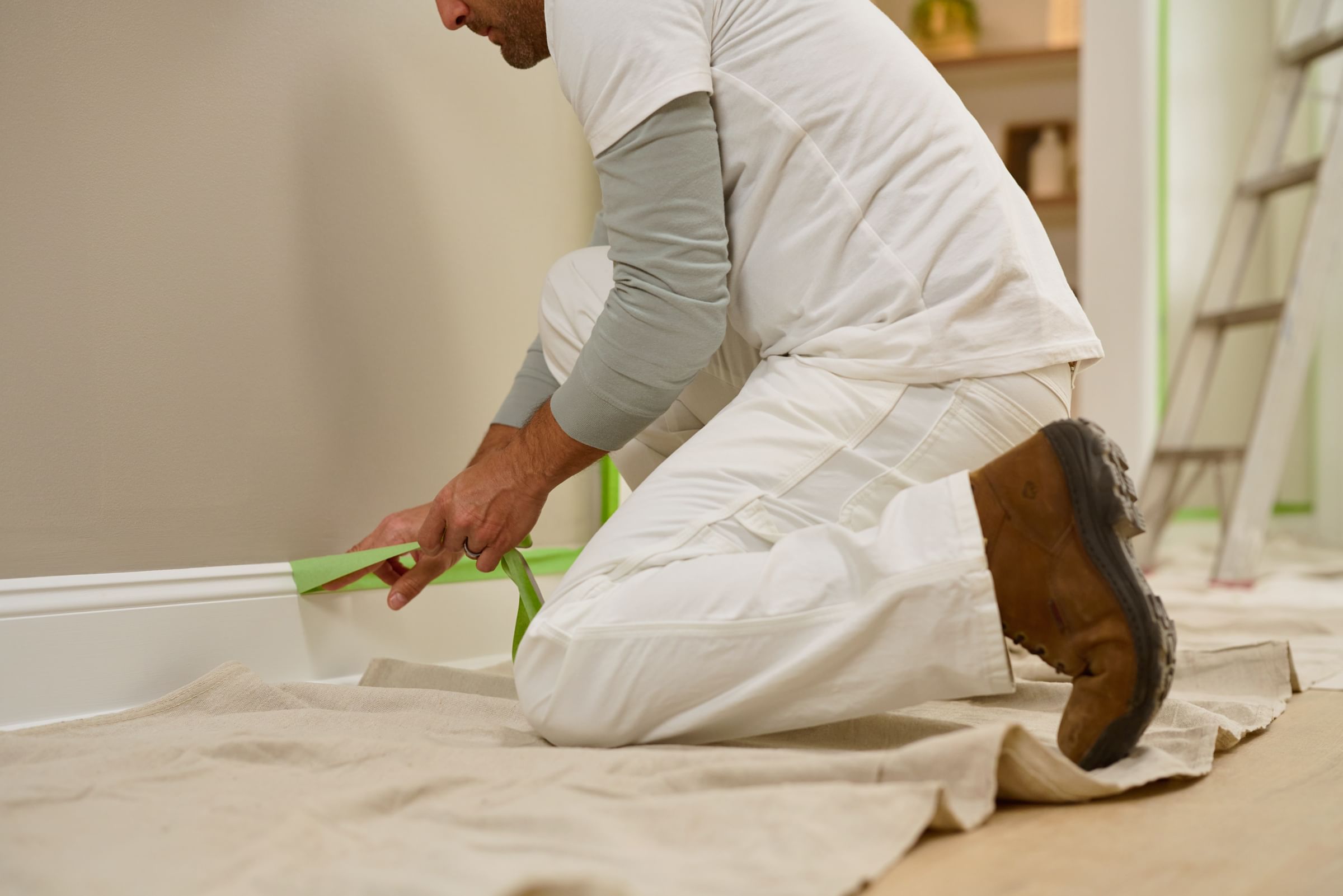 A man peeling Green FrogTape Multi-Surface Painter's Tape off of baseboard trim