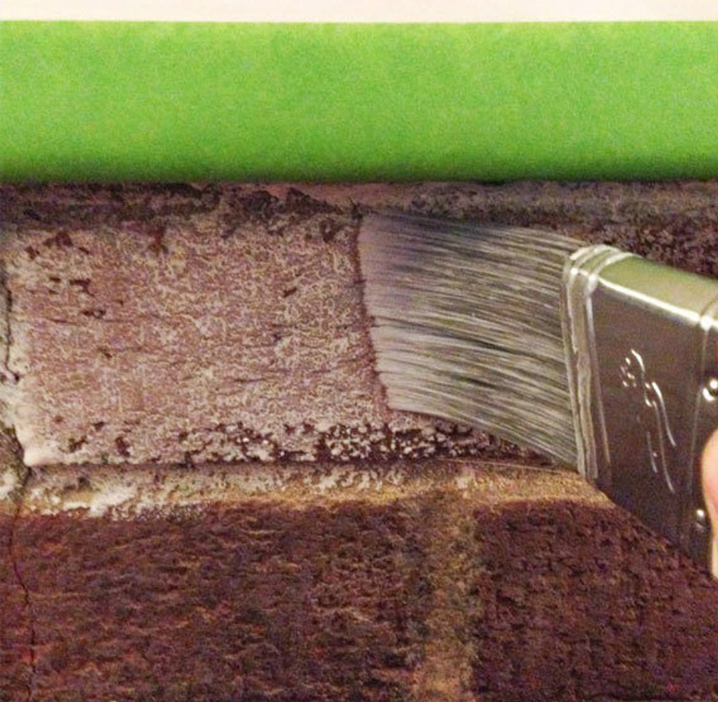 Paint brush whitewashing brick. The brick is taped off with Green FrogTape Multi-Surface Painter's Tape