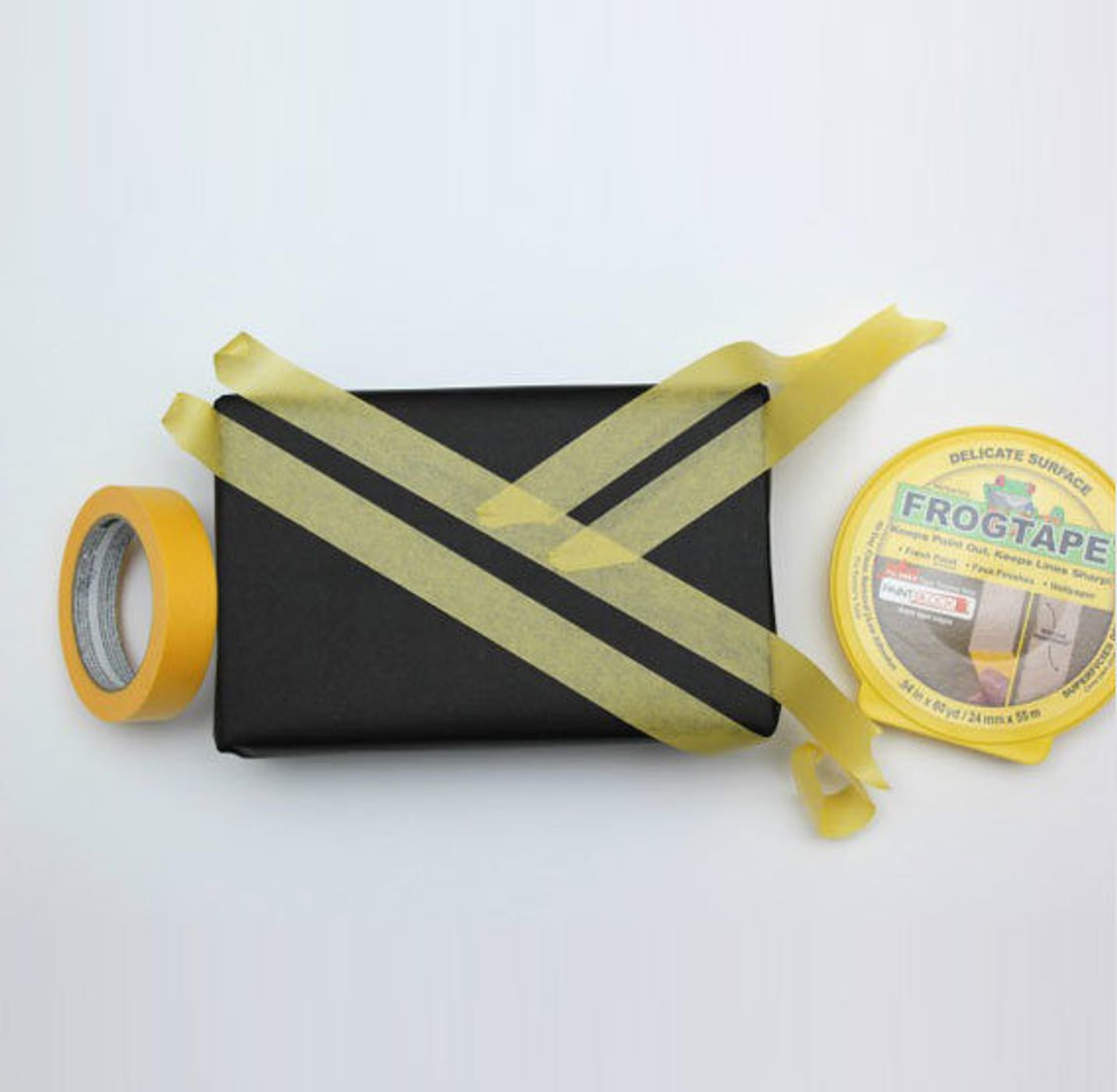 Little black rectangular box with strips of Yellow FrogTape Delicate Surface Painter's Tape on it. There is a roll of the tape on the left and the tape canister on the right