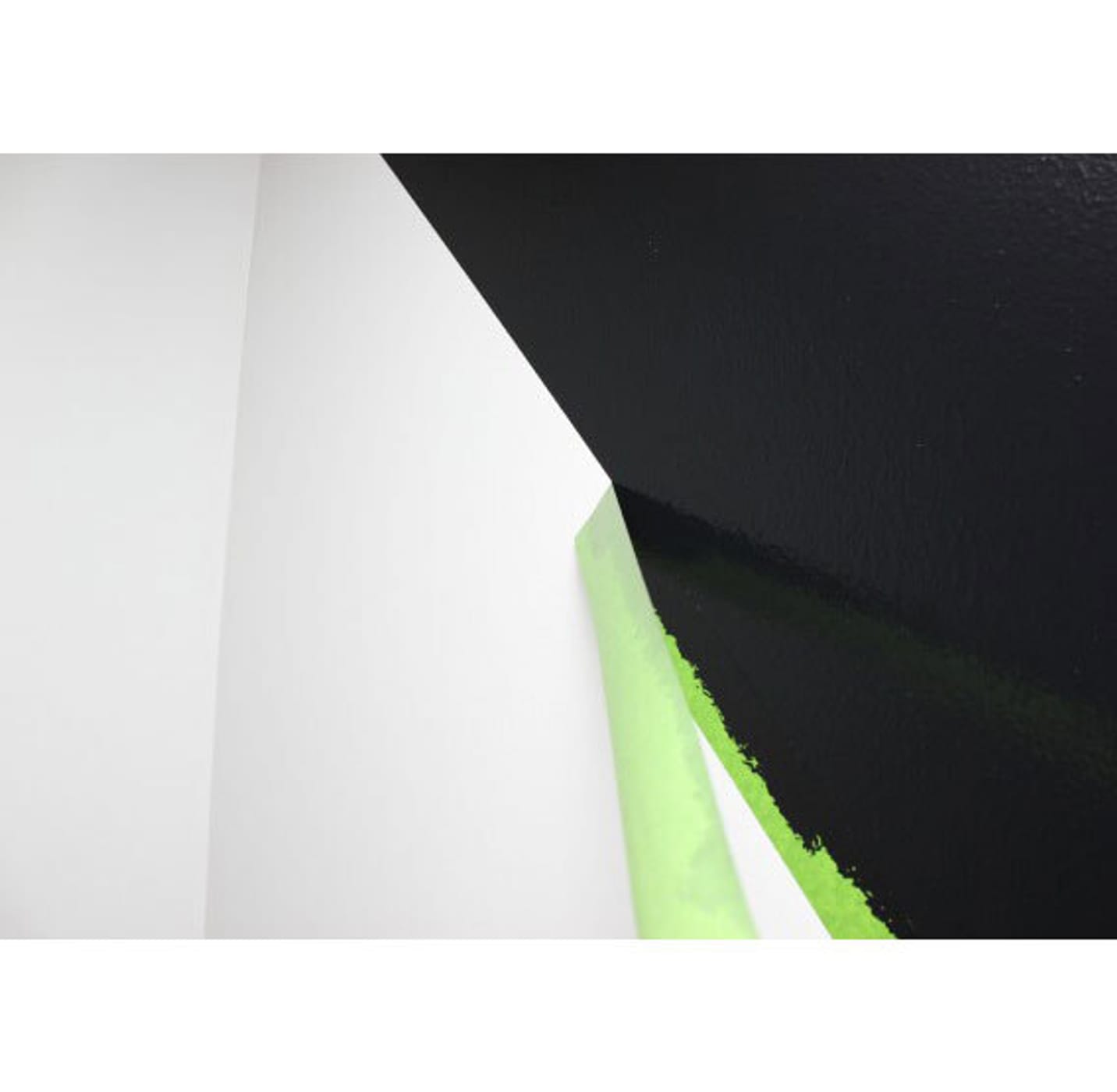 Green FrogTape Multi-Surface Painter's Tape being peeled off of a wall. The tape is creating a crisp line on a wall between the black and white side of the wall.
