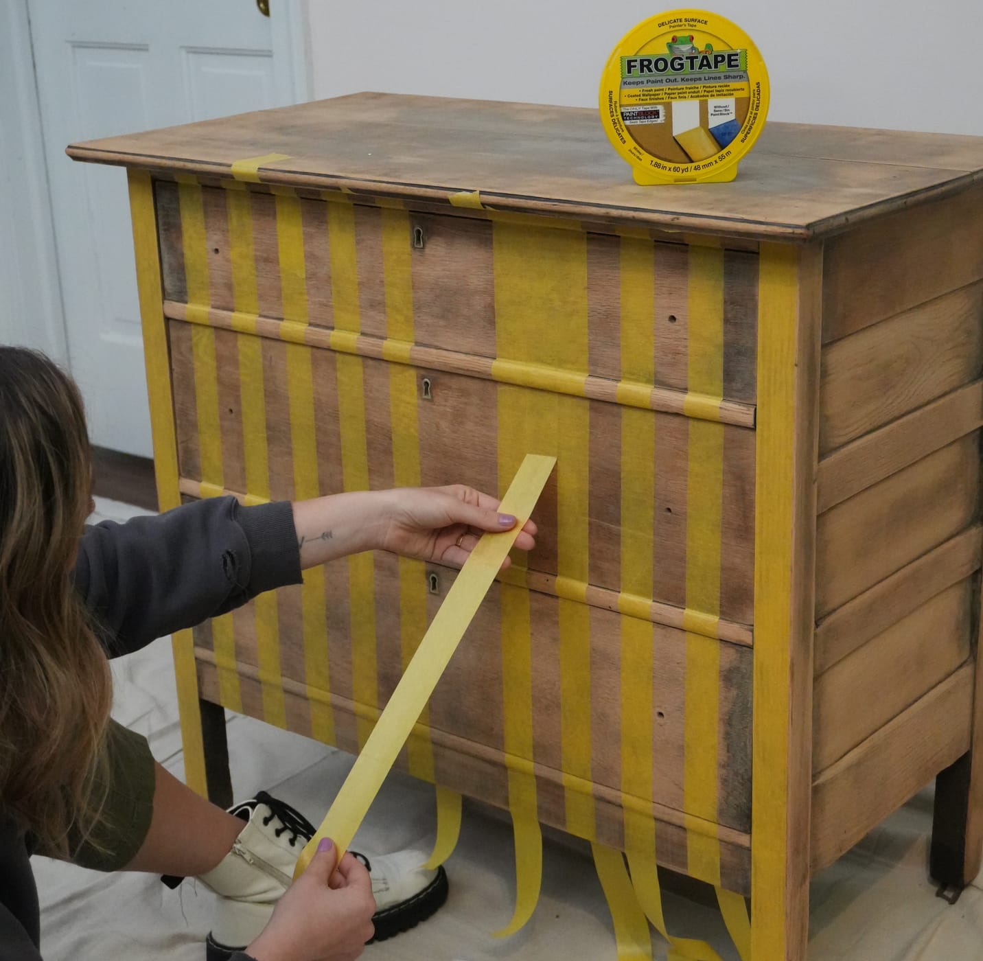 A woman using Yellow FrogTape Delicate Surface Painter's Tape to Tape vertical stripes on an old dresser