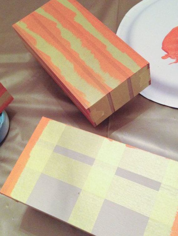 Two Wooden Blocks with Yellow FrogTape Delicate Surface Painter's Tape on them. The one is painted with orange paint and the other is just starting to be painted