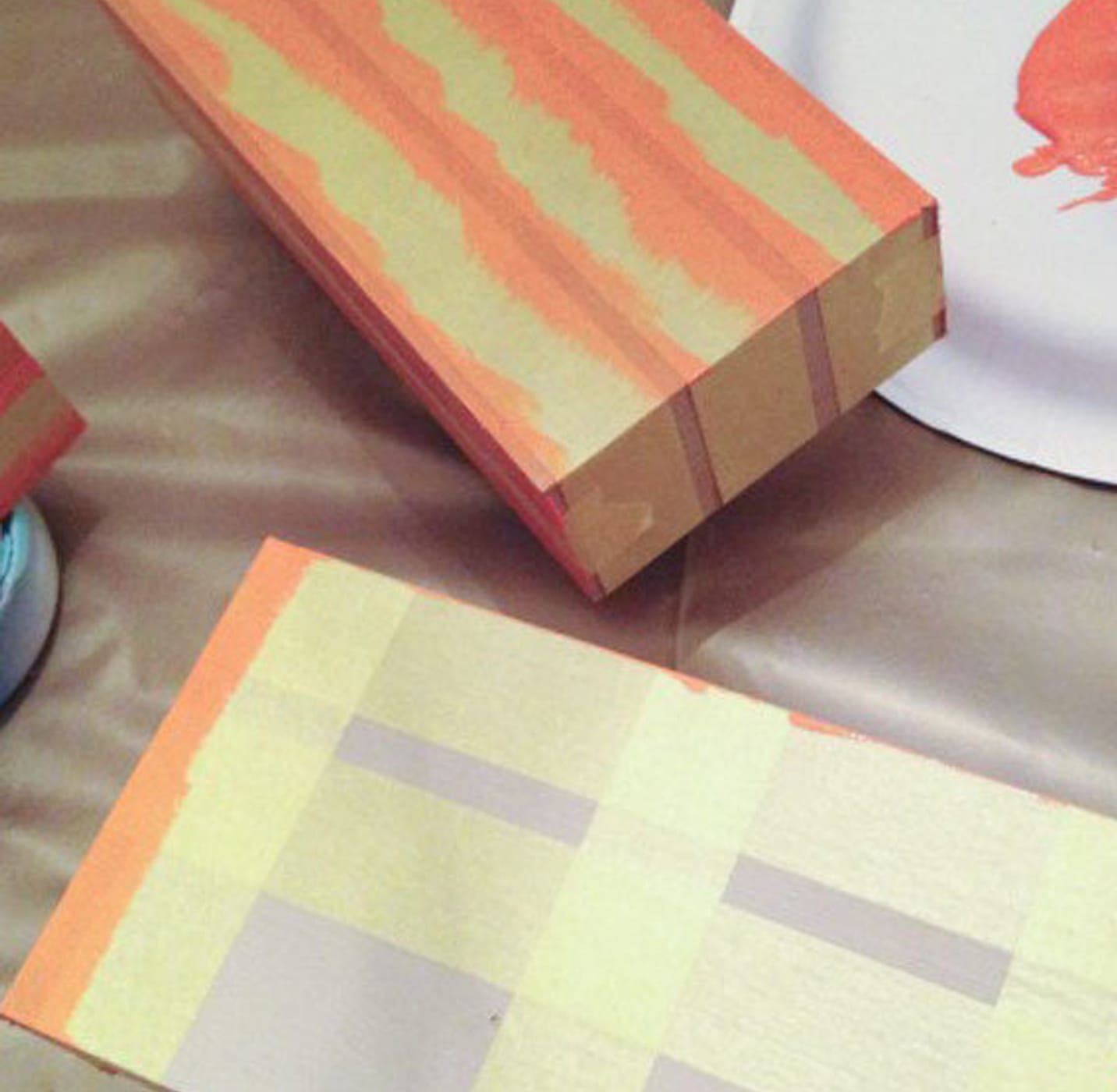 Two Wooden Blocks with Yellow FrogTape Delicate Surface Painter's Tape on them. The one is painted with orange paint and the other is just starting to be painted