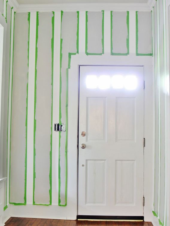 White entryway door. The wall is taped from ceiling to floor with spaced out Green FrogTape Multi-Surface Painter's Tape. The wall stripes are alternating gray and white.