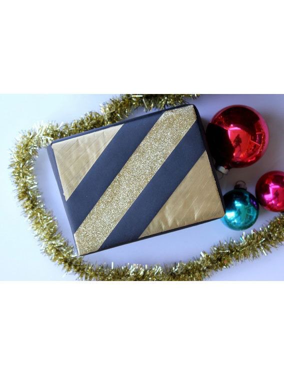 Little black and gold box in the middle of gold garland and three ornament bulbs (2 red and one green)