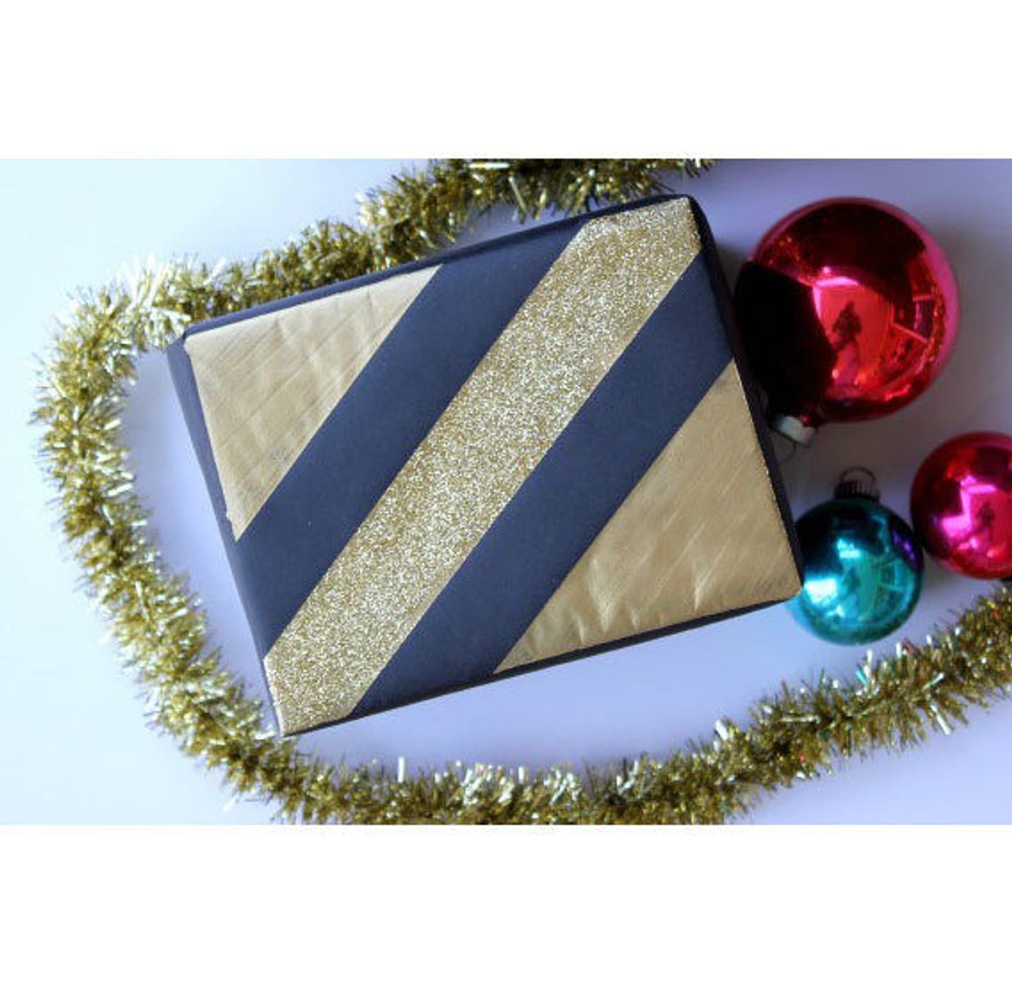 Little black and gold box in the middle of gold garland and three ornament bulbs (2 red and one green)