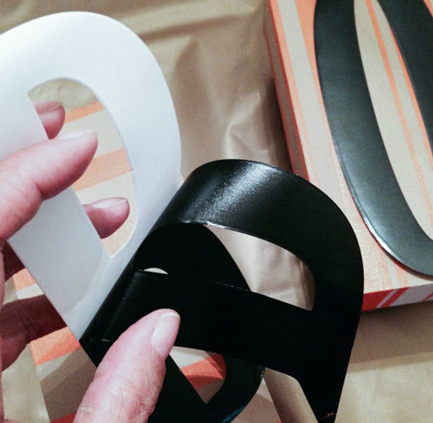 A decal of the letter B being peeled off of the backing. The letter O is on a block in the background.