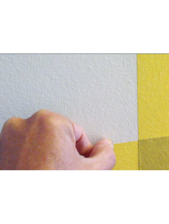 Hand Taping Yellow FrogTape Delicate Surface Painter's Tape on a white wall