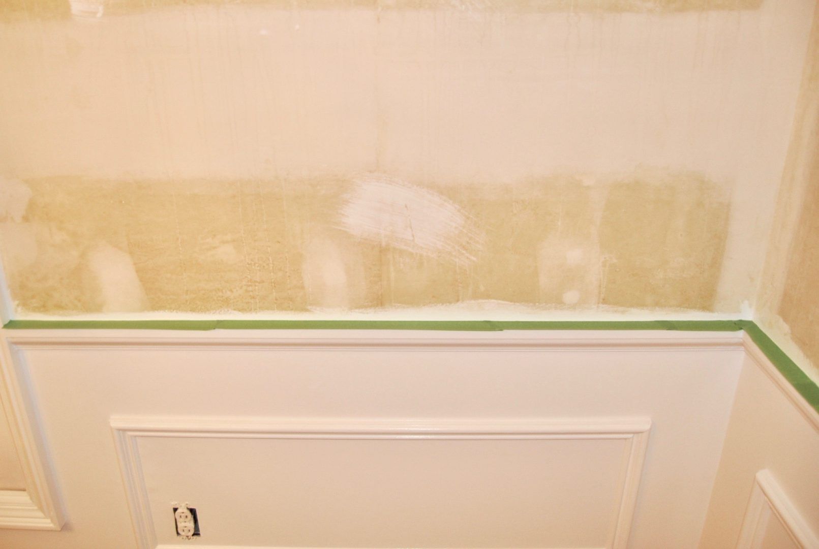 Green FrogTape Multi-Surface Painter's Tape masked on the trim of the white wainscotting on a wall.