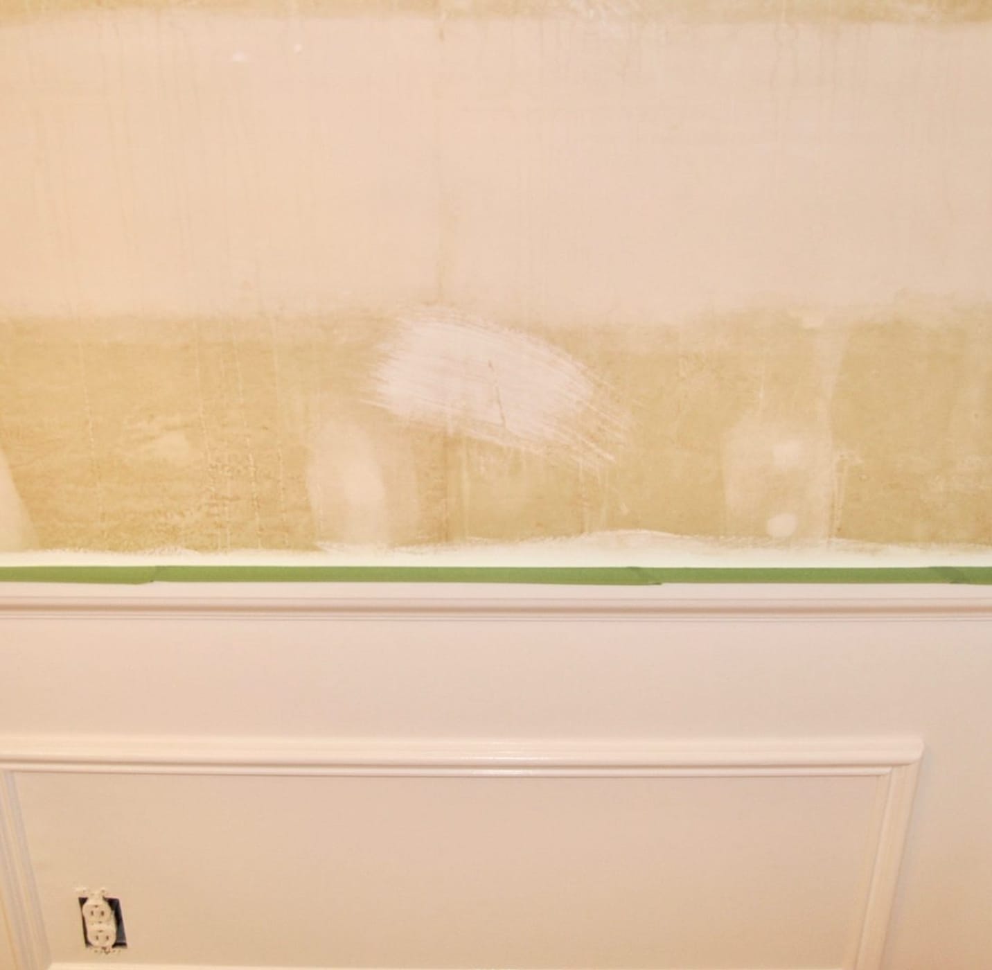 Green FrogTape Multi-Surface Painter's Tape masked on the trim of the white wainscotting on a wall.