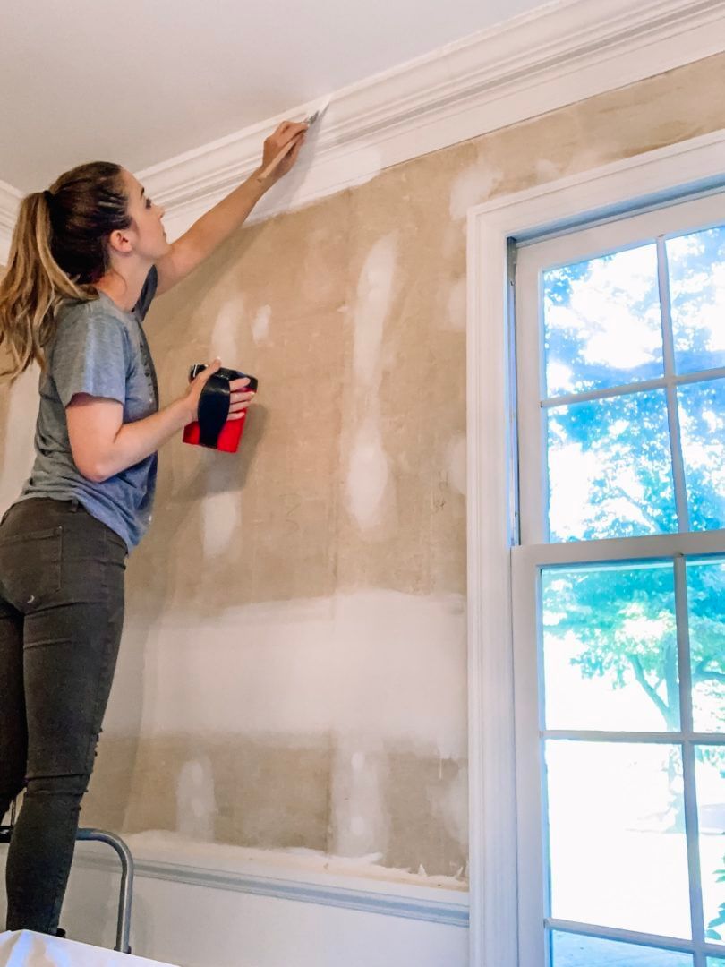Woman on a step ladder painting the ceiling trim white.