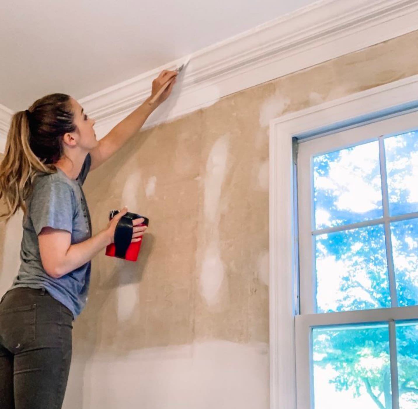 Woman on a step ladder painting the ceiling trim white.