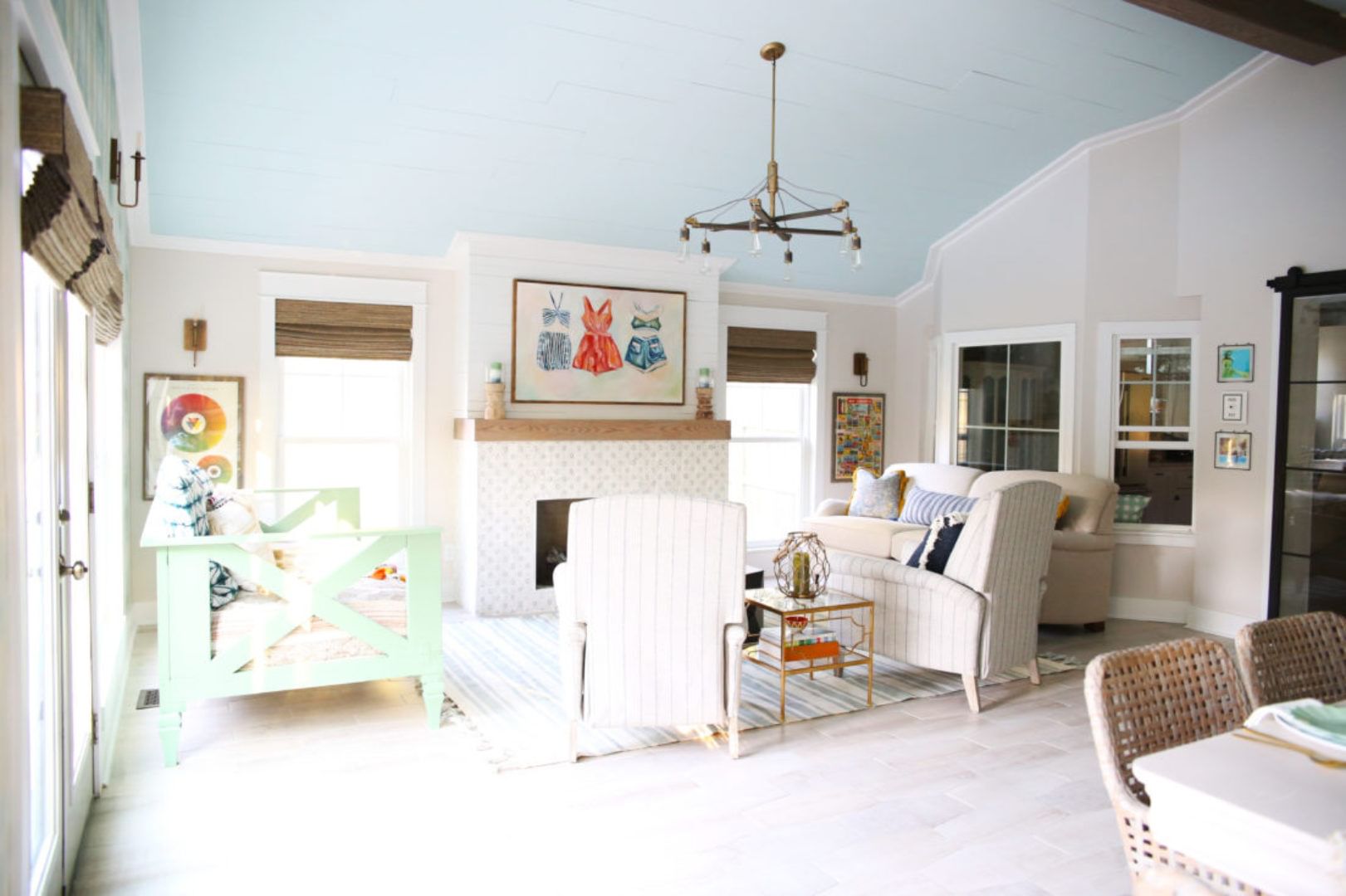 Living room with white chairs, a white fireplace with a painting of clothing over the mantle, and two small couches