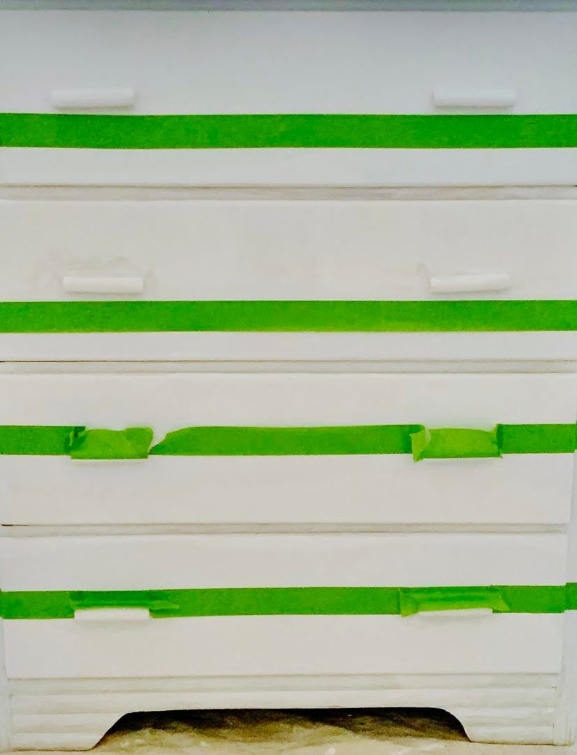 Four strips of Green FrogTape Multi-Surface Painter's Tape taped horizontally on a white dresser