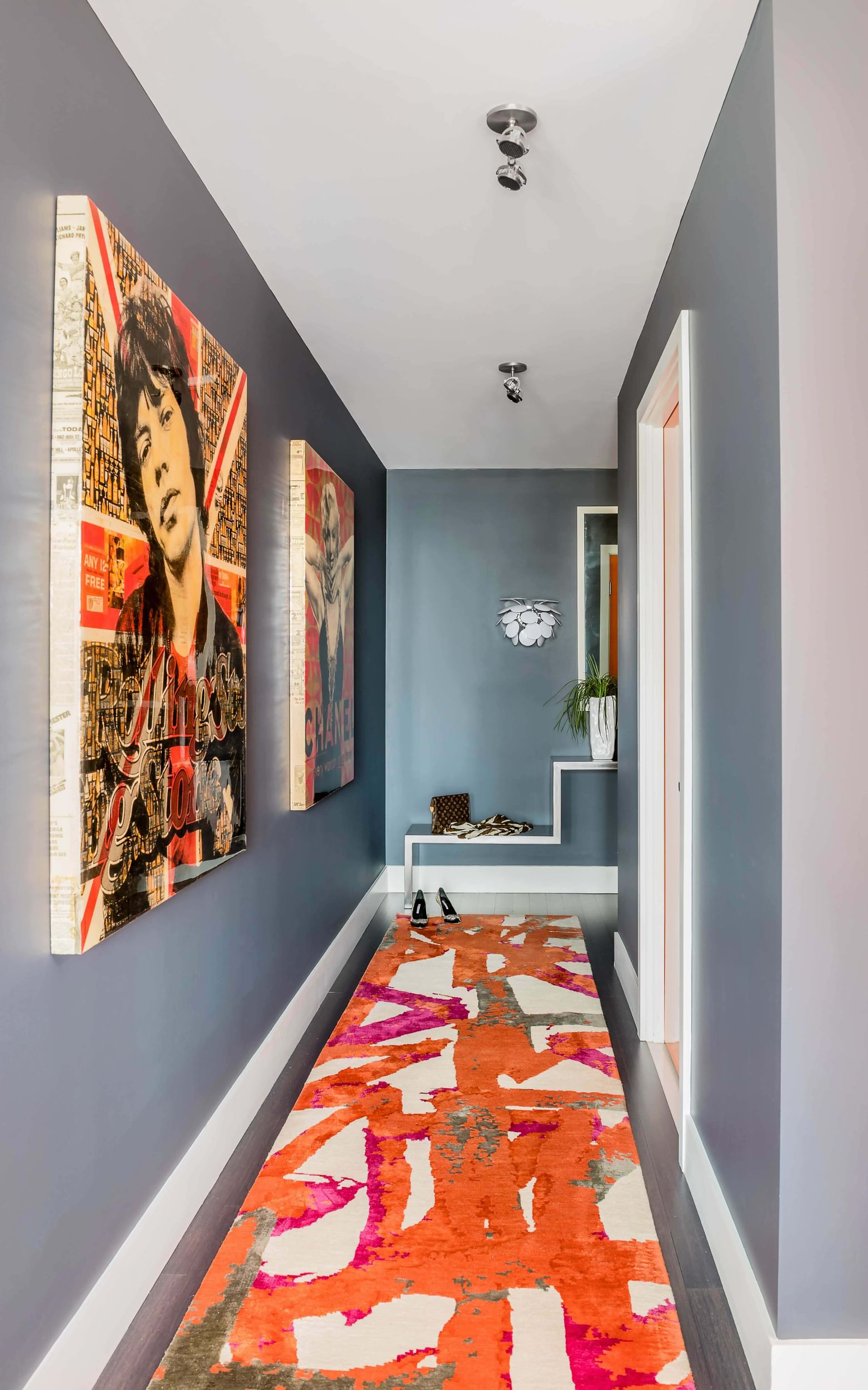 Short hallway in a home with artwork on the walls, and a long patterned carpet colored orange, fushia, and white.