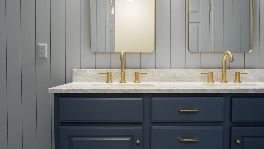 Blue bathroom cabinets with gold sink hardware, mirrors, and accents, sitting on a black and white tile floor