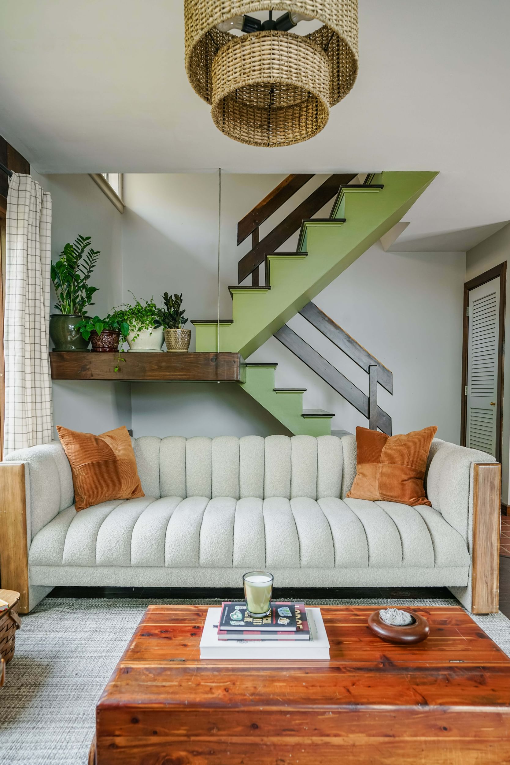 70's inspired room with cream colored couch with orange throw pillows, a wooden coffee table, and freshly painted green staircase with brown railings, landing, and steps.