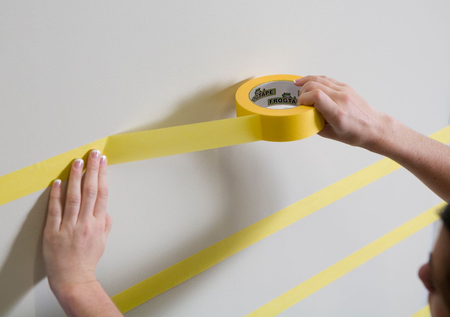 Horizontal Strips of Yellow FrogTape Delicate Surface Painter's Tape being applied to a white wall