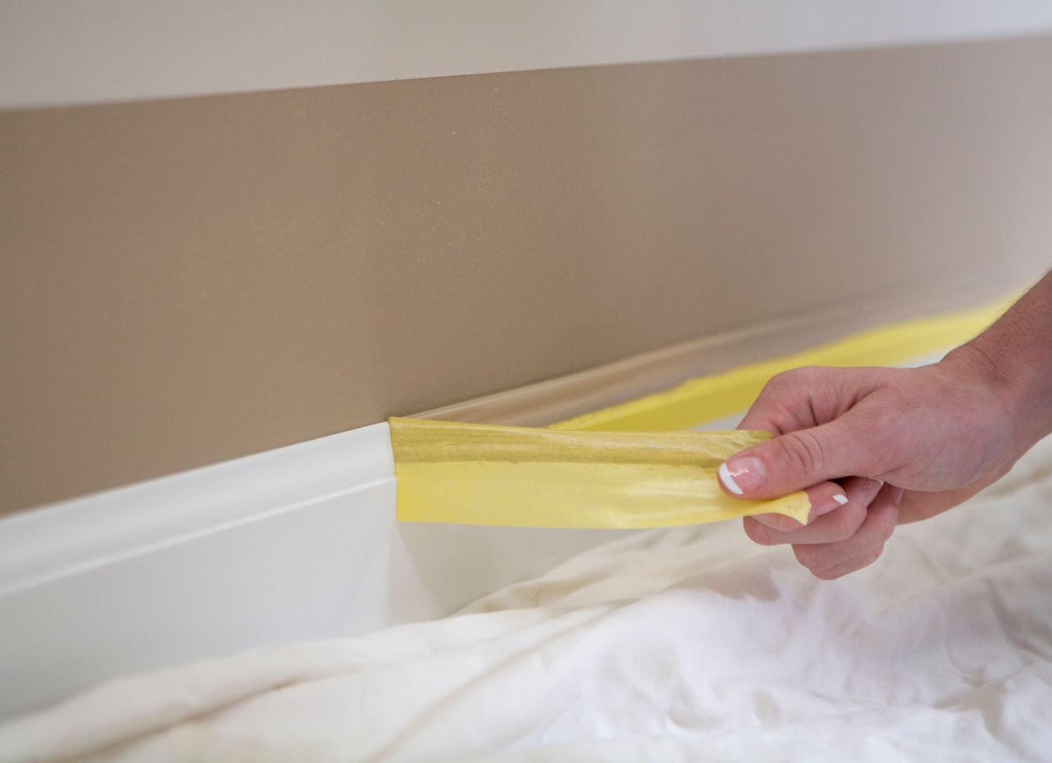 Yellow ForgTape Delicate Surface Painter's Tape being peeled off of white baseboard trim to reveal a crisp line between the brown wall and white trim