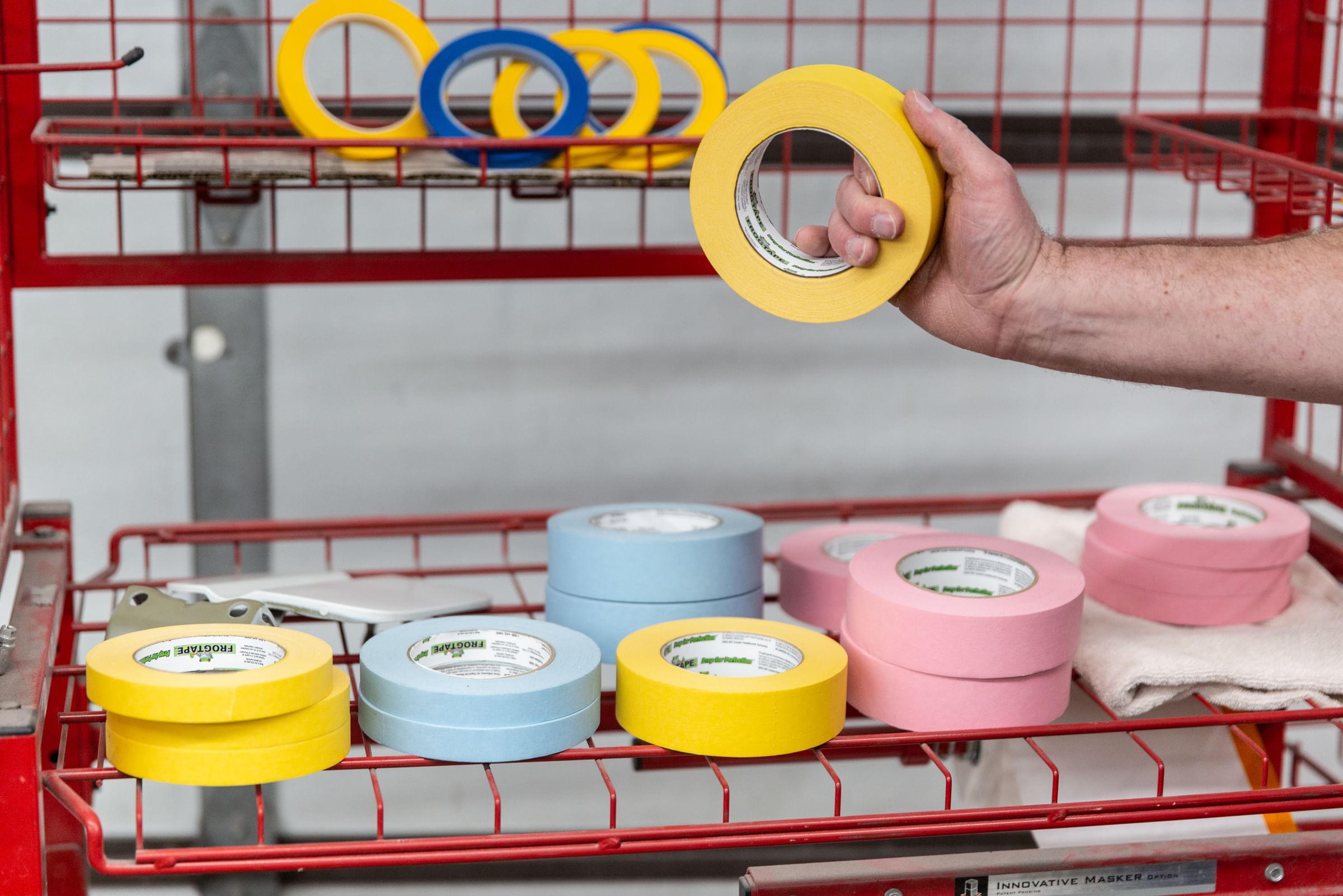 Mulitple different colors of FrogTape Performance masking tape on an orange wire rack shelf.