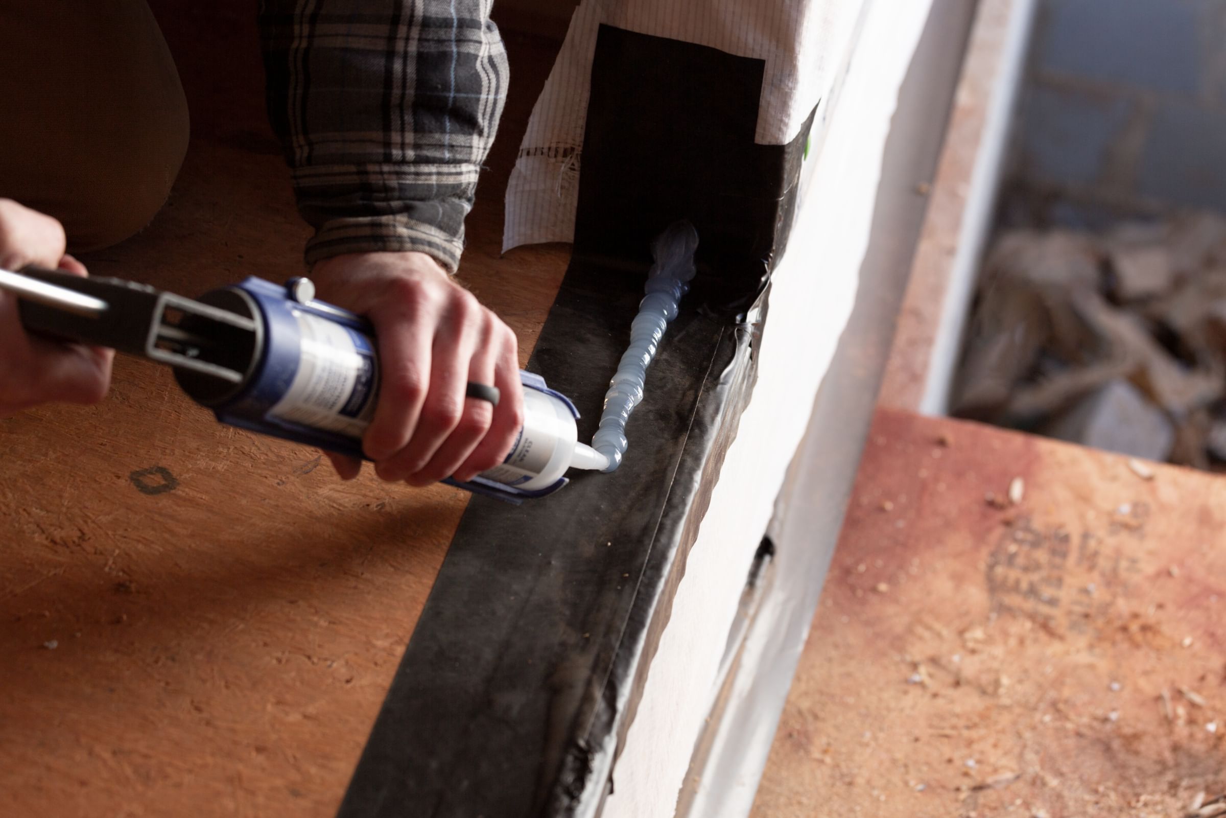 A man applying Caulk over FrogTape Flashing Tape