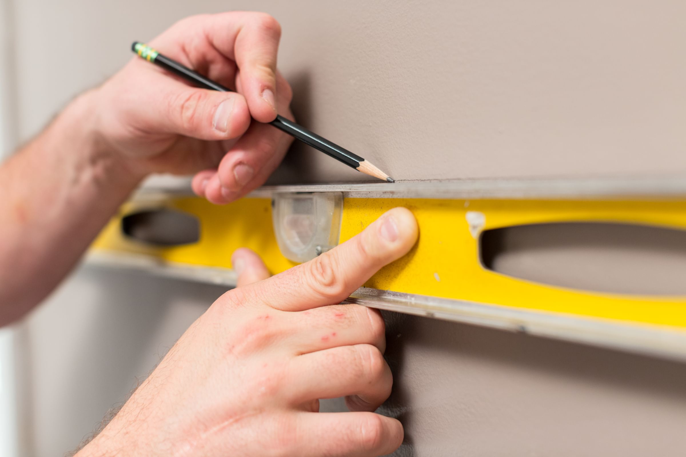 A person using a level to draw a line on a wall with a pencil