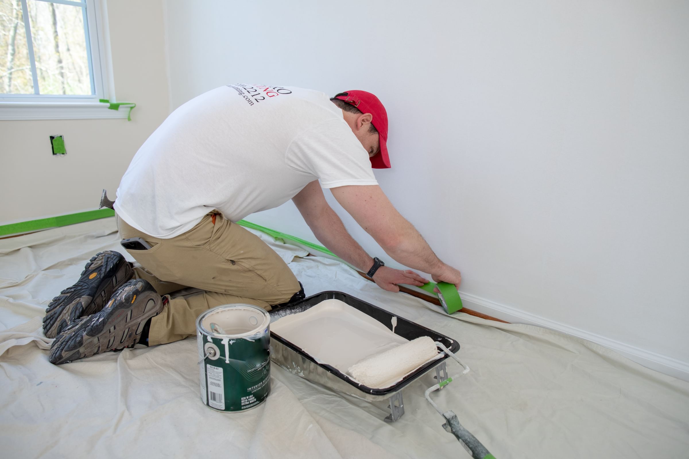 A painter masking off baseboard trim using Green FrogTape Multi-Surface Painter's Tape.
